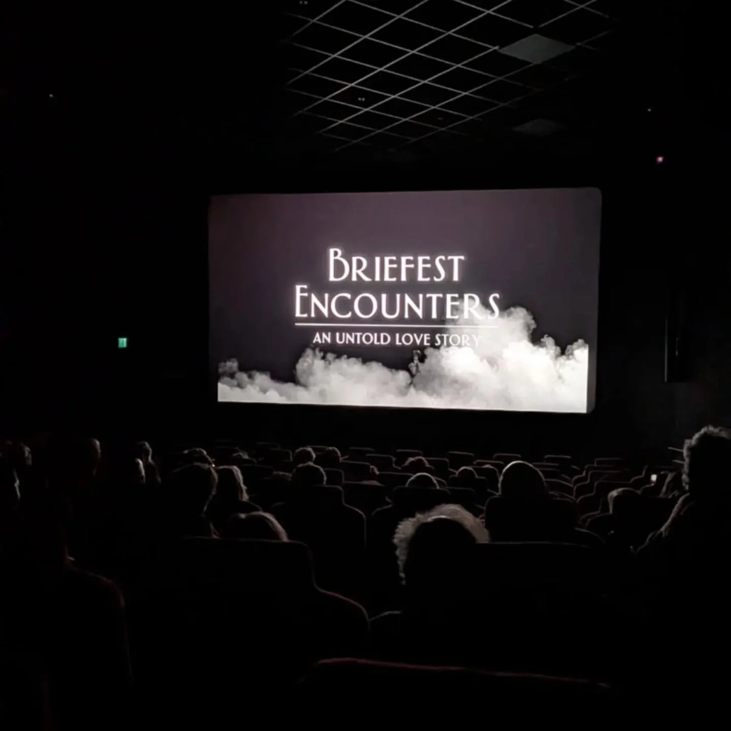 Movie theater showing a screen with the title "Briefest Encounters: An Untold Love Story" against a background of clouds.