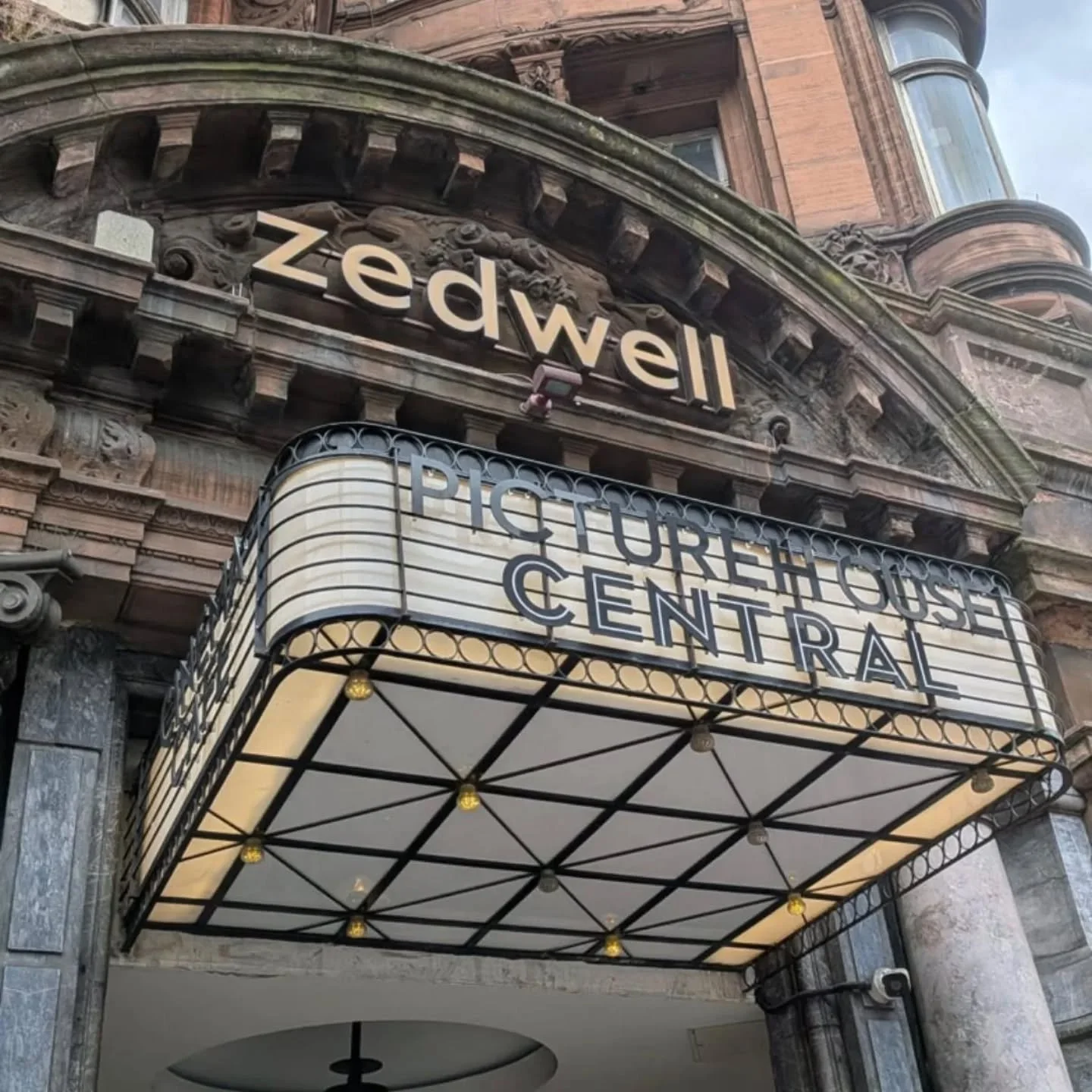Historic theater entrance with ornate stone facade, marquee sign reading "Picthouse Central," and a rounded canopy with decorative metalwork.