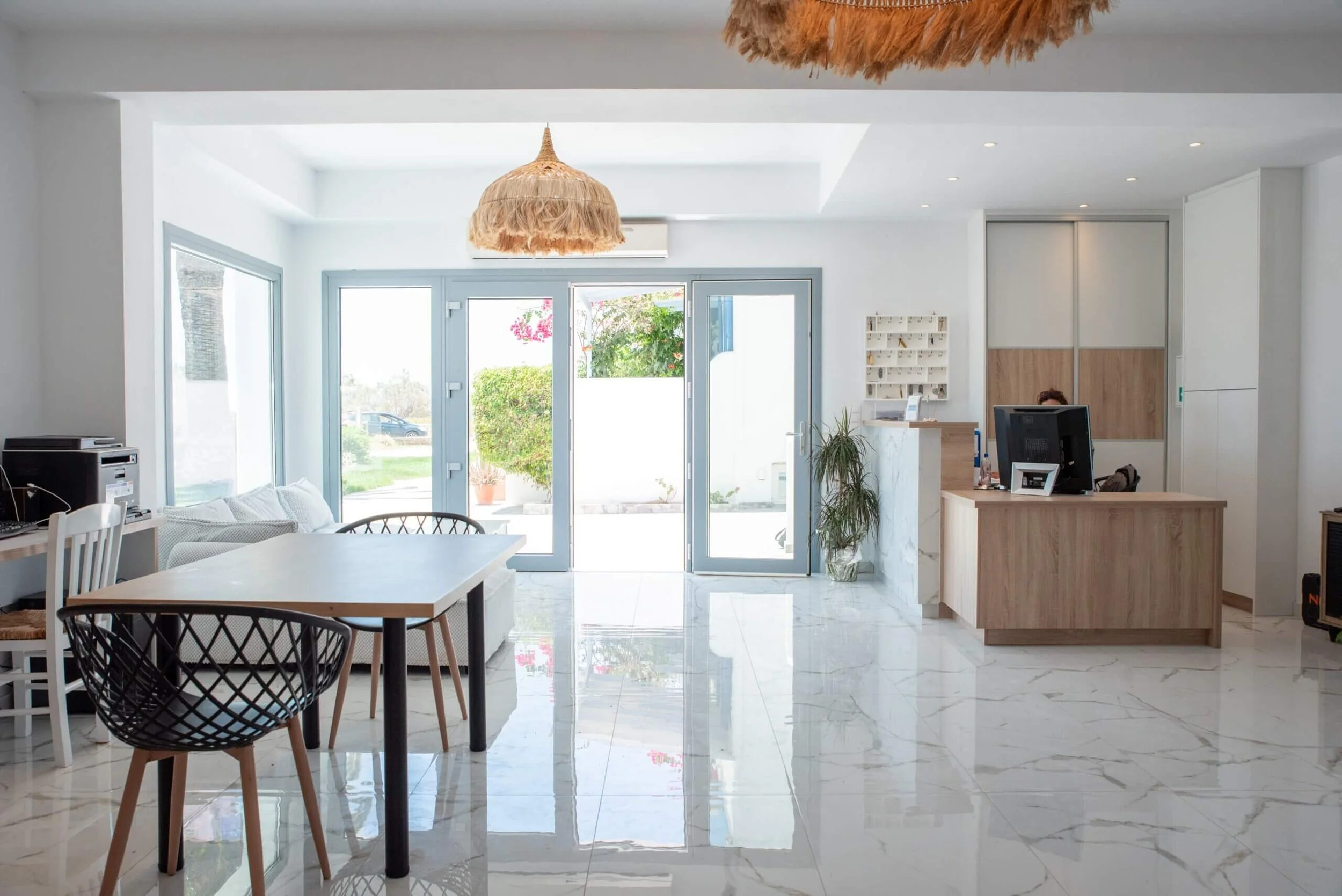 Bright living room with large glass doors, white walls, tiled floor, wooden furniture, greenery outside, and modern decor.