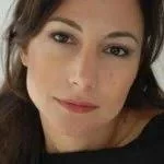 Close-up of a woman with dark hair and light makeup, lying down and looking at the camera.