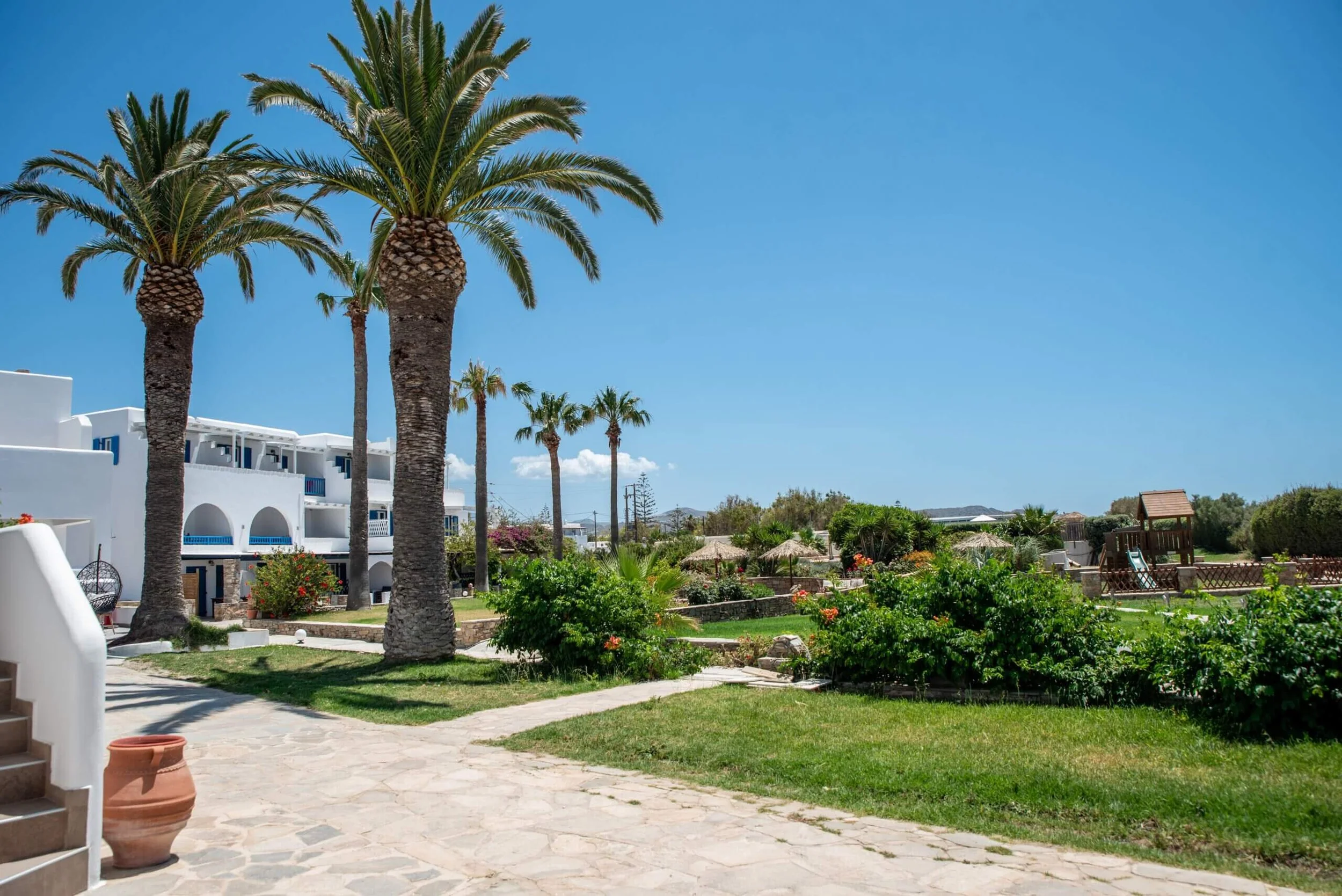 Beautiful resort with tall palm trees, white buildings with blue accents, a lush green garden, and a clear blue sky.