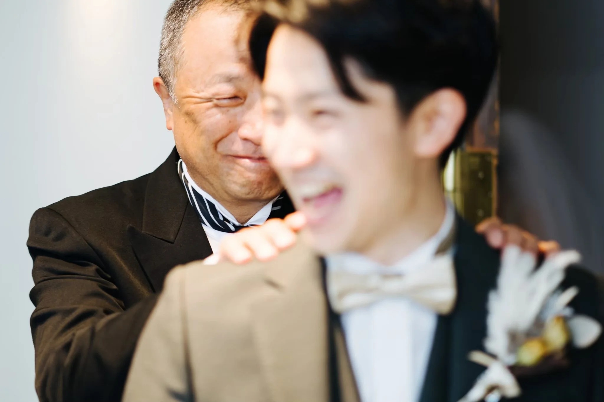 Two men with different ethnic backgrounds smiling and leaning close to each other while looking at a bouquet of flowers.