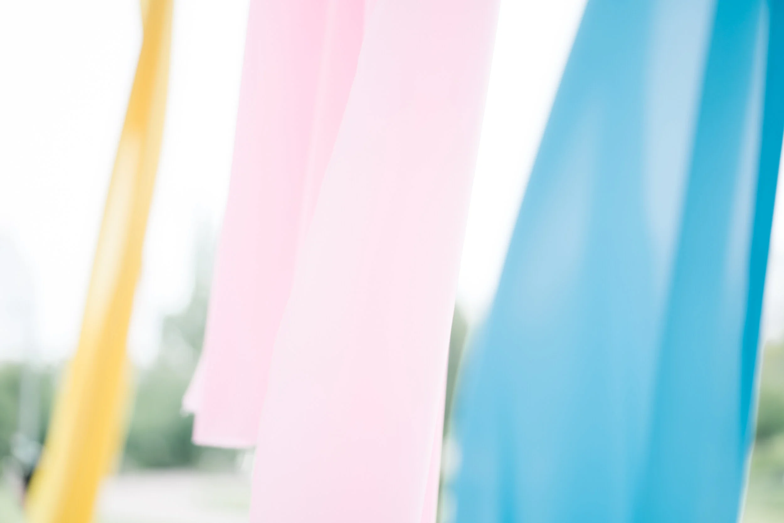 Close-up of pastel-colored paper cutouts or fabric strips in yellow, pink, blue, and green hanging outdoors.