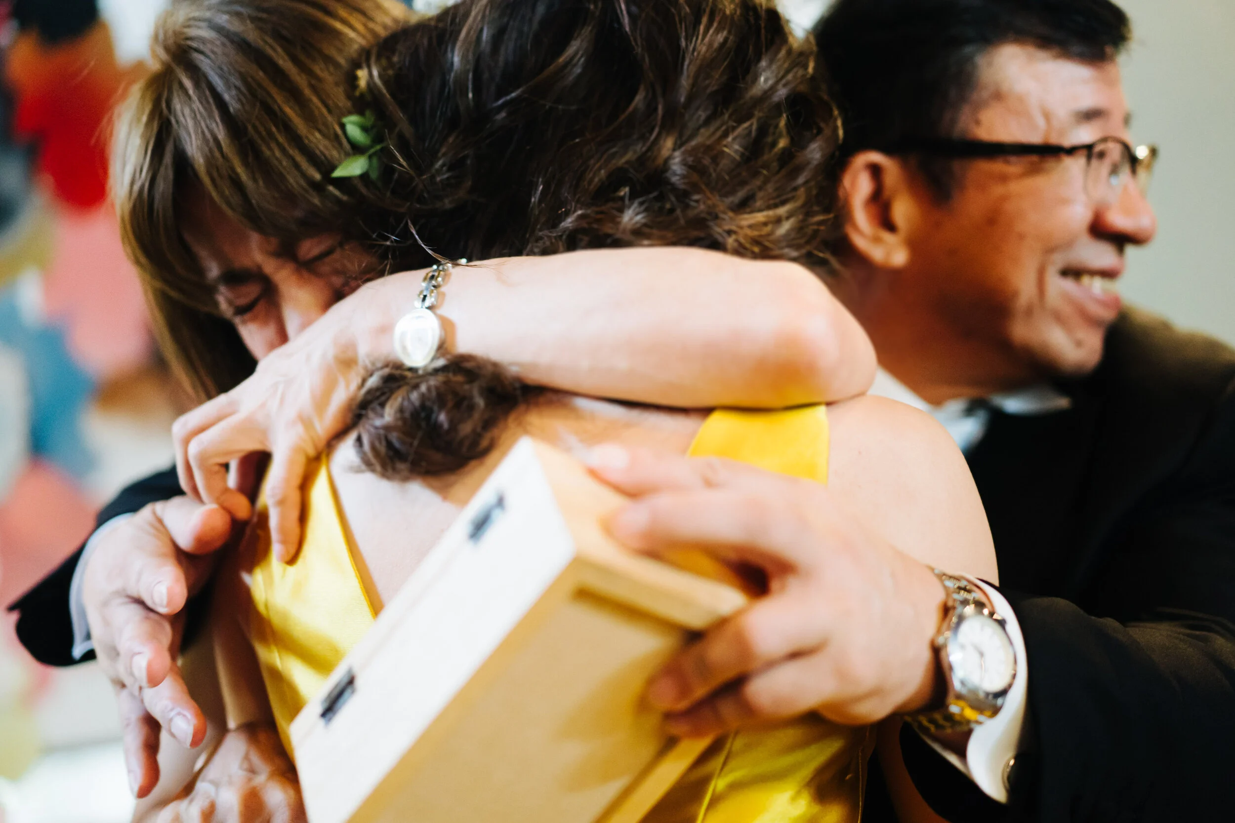 Two women hugging each other tightly, one wearing a yellow tank top and the other wearing a white shirt with black details, in a warm embrace.