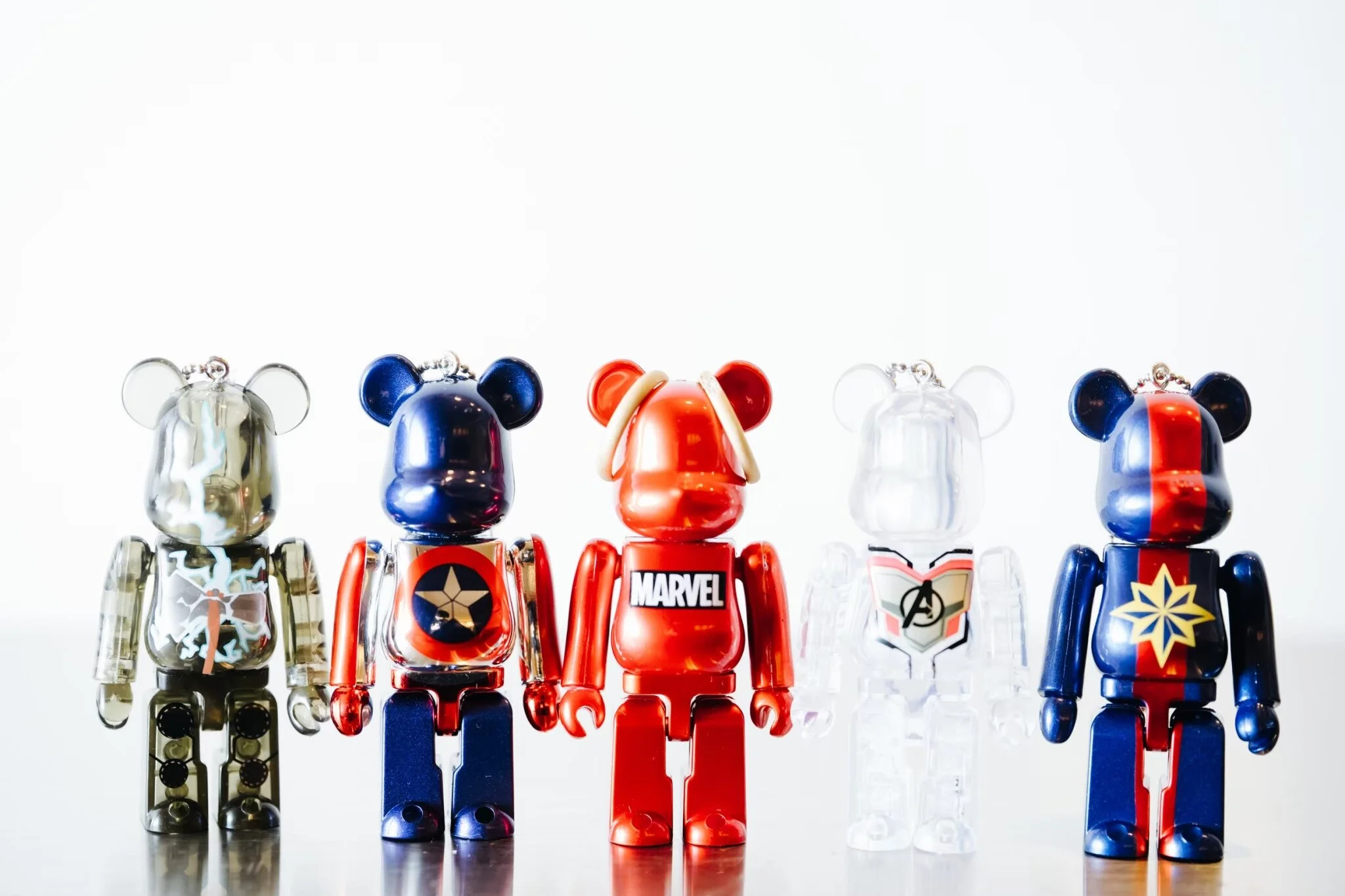 Five colorful toy robotic figures resembling superheroes or comic characters, lined up in a row against a white background.