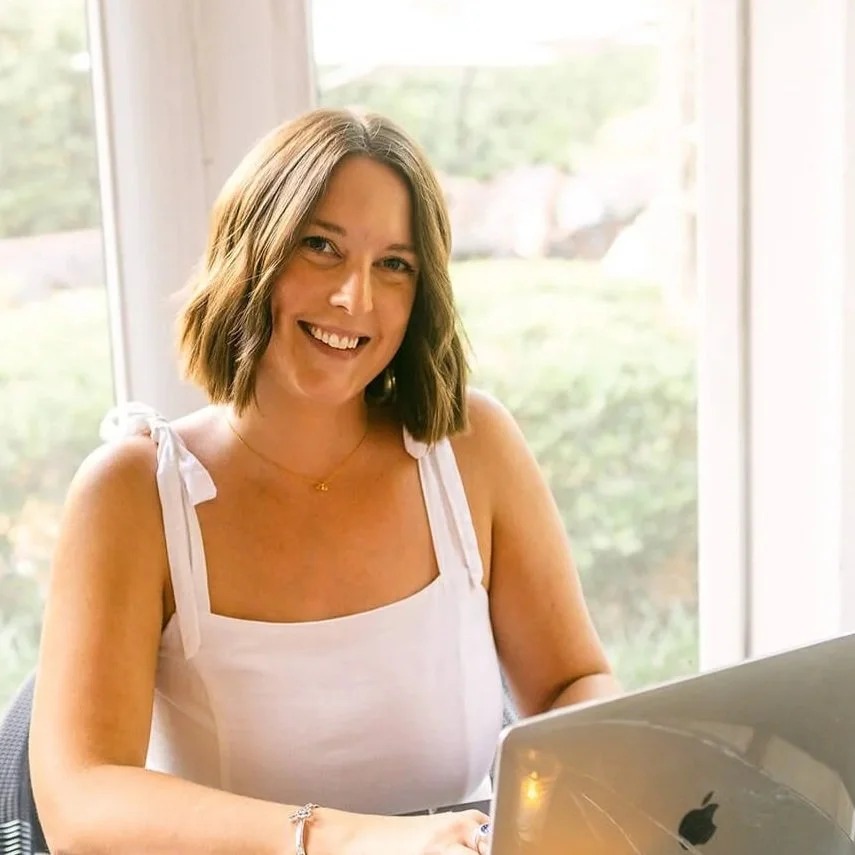 Polly Clover, website copywriter, typing on laptop and smiling at camera
