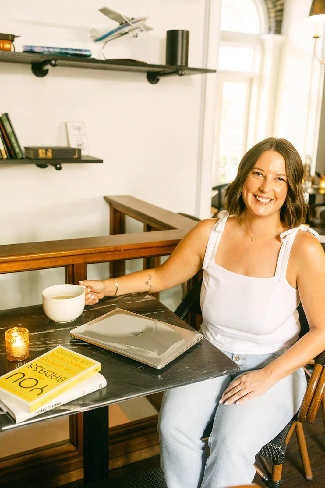 Polly Clover, a freelance writer, smiling and sitting at a bistro table with laptop and coffee cup.