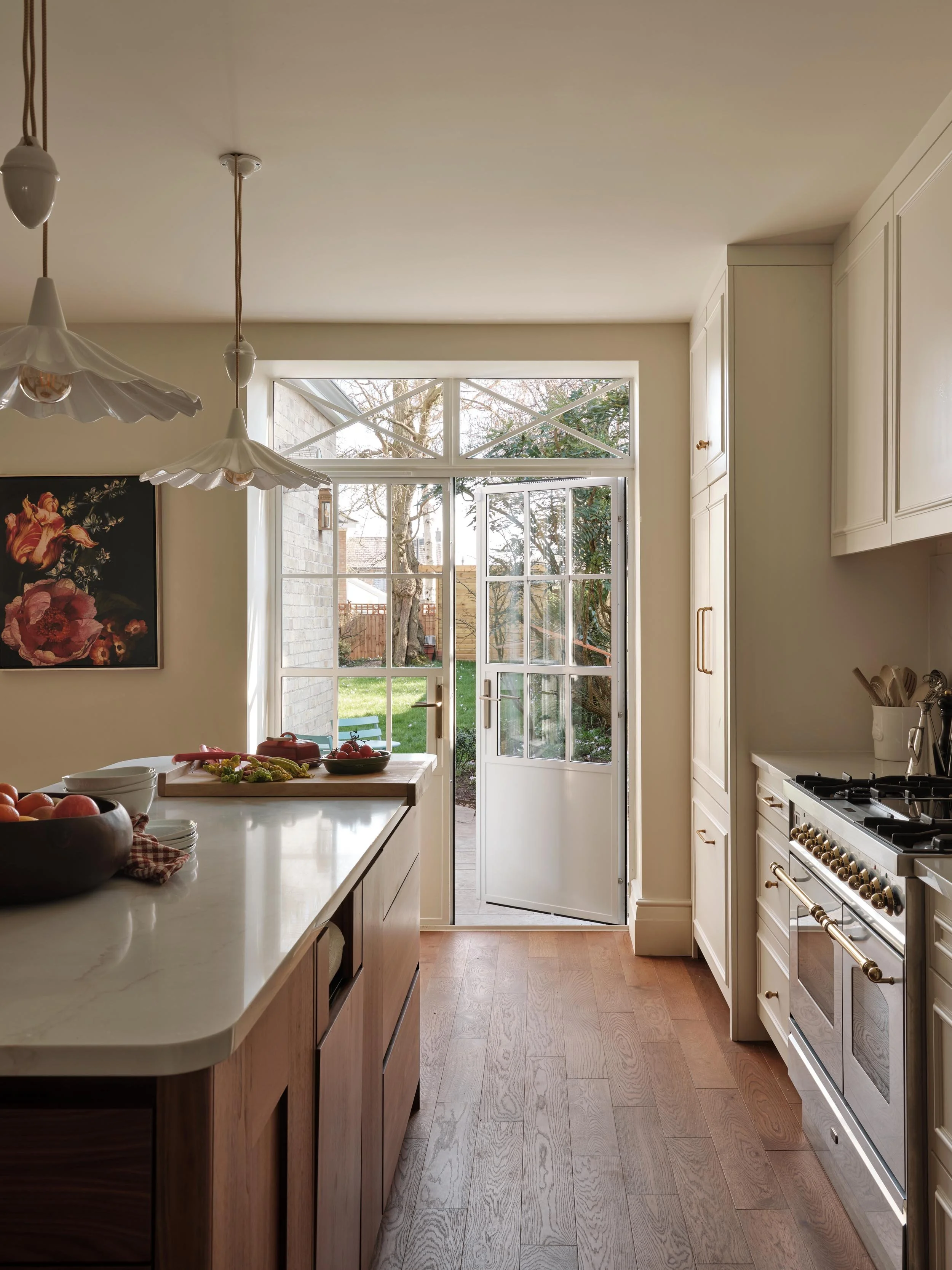 A bright kitchen with a window door leading to the backyard, white cabinetry, and a white countertop with bowls of fruit on it.
