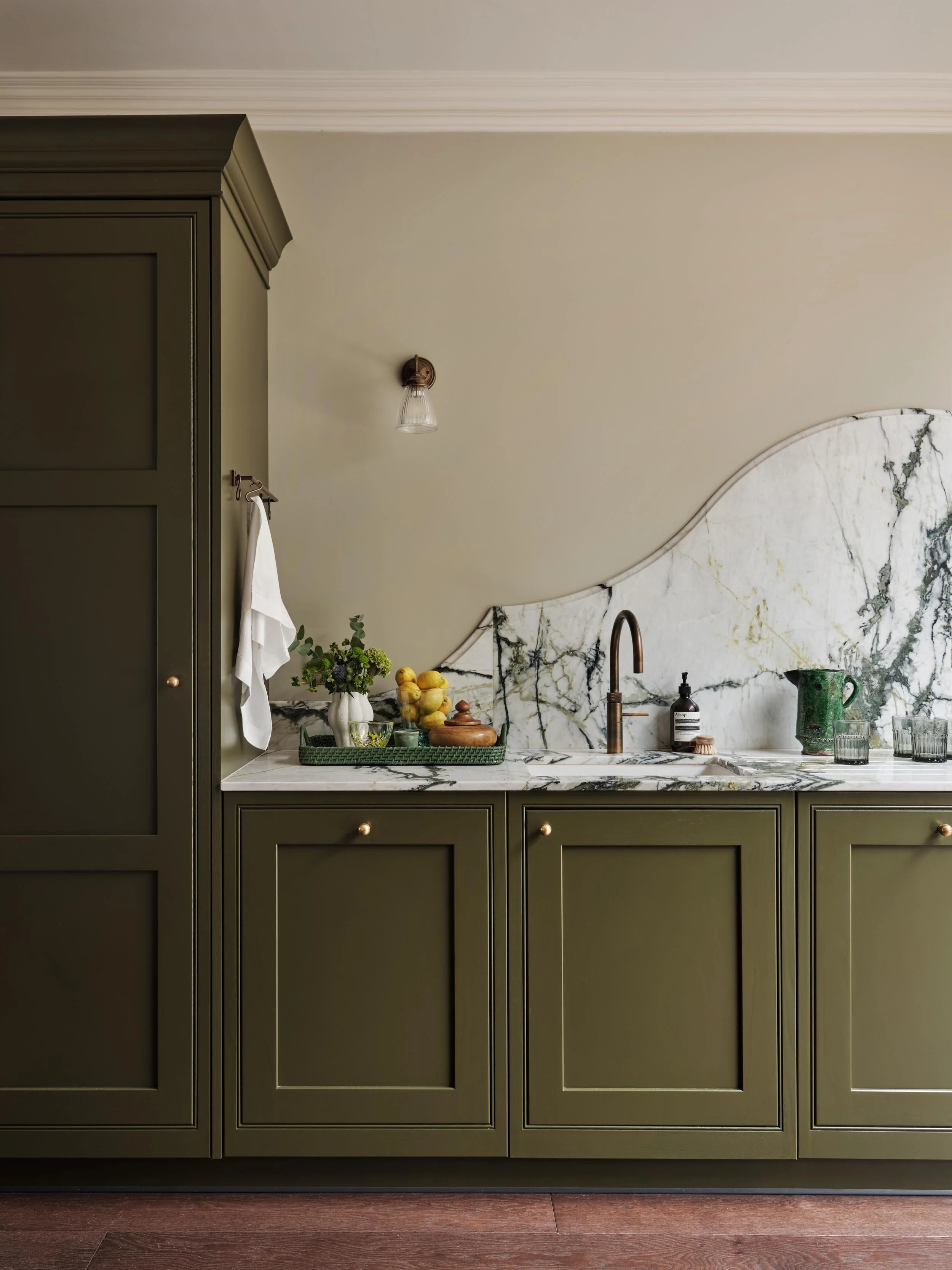 Green kitchen cabinets with marble countertop and backsplash, providing a modern and elegant look.