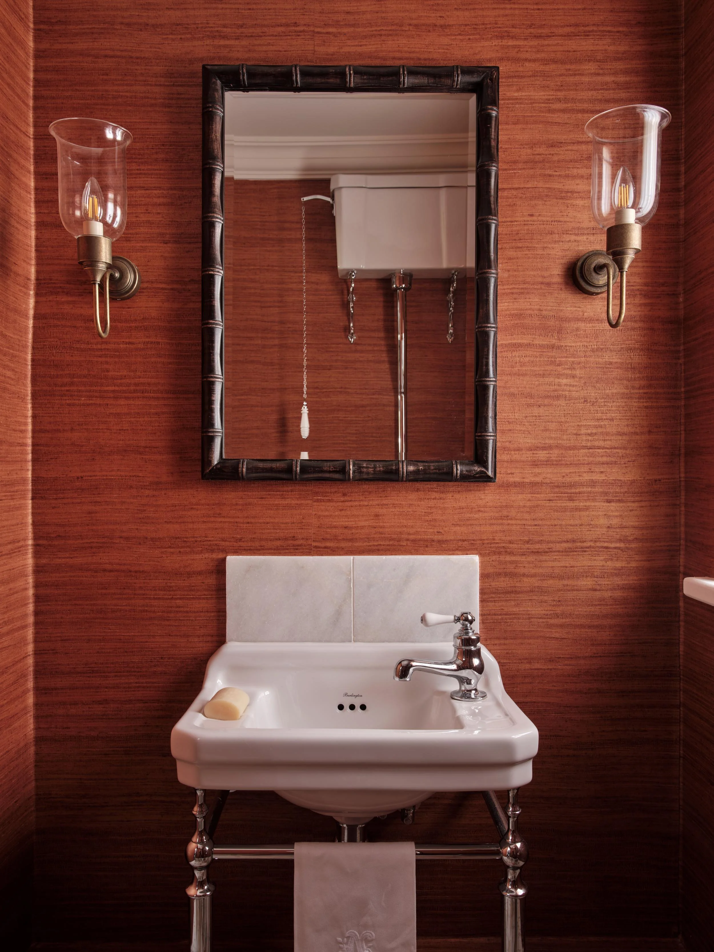 A bathroom with a white sink, a mirror, and wall-mounted vintage-style sconces with glass shades on a wood-paneled wall.