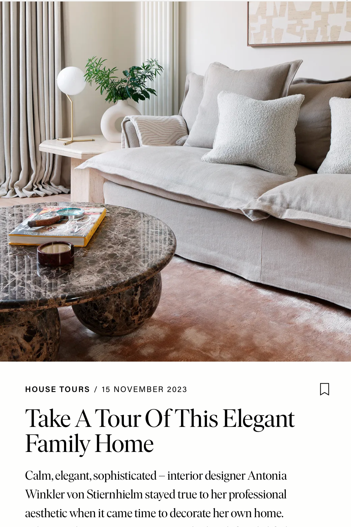 A modern living room with a beige sofa, white pillows, a marble coffee table, a plant, a white table lamp, and beige curtains.