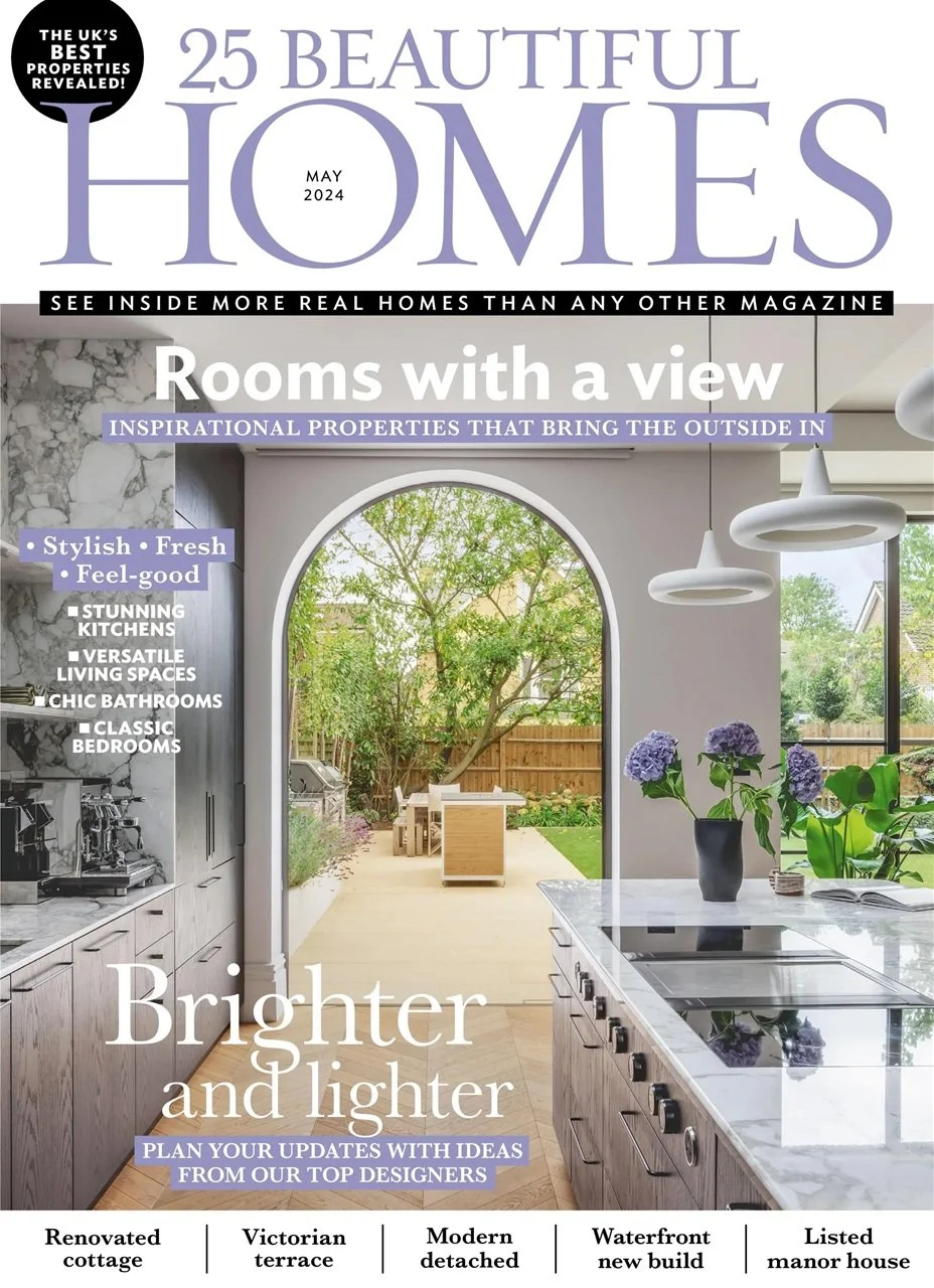 Magazine cover titled '25 Beautiful Homes, May 2024'. The cover features a bright kitchen view looking out to a backyard with green trees and outdoor furniture through a large arched doorway. The kitchen has marble countertops, modern appliances, and purple flowers on the counter.