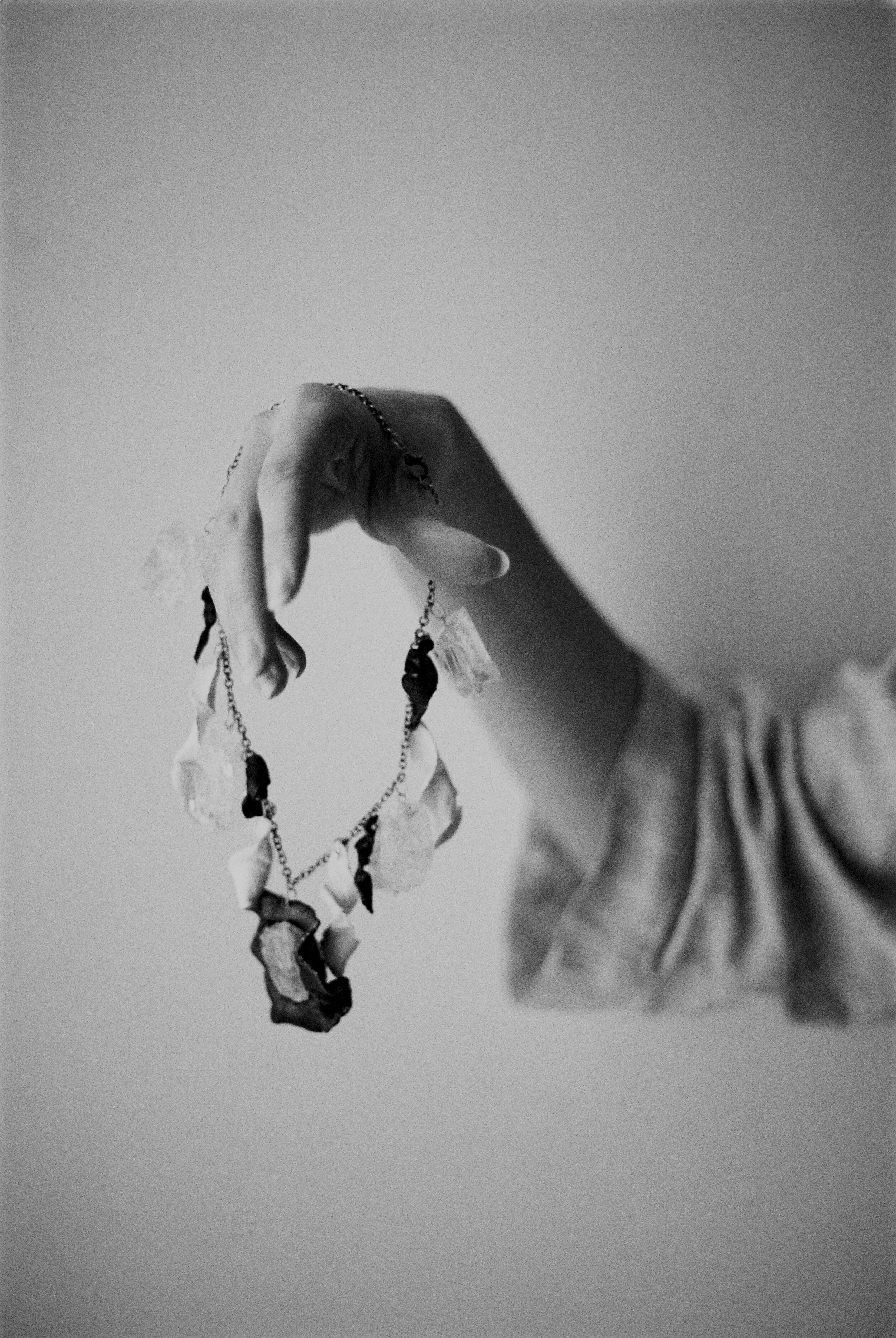 Hand holding a necklace with black and white stones against a plain background in black and white.