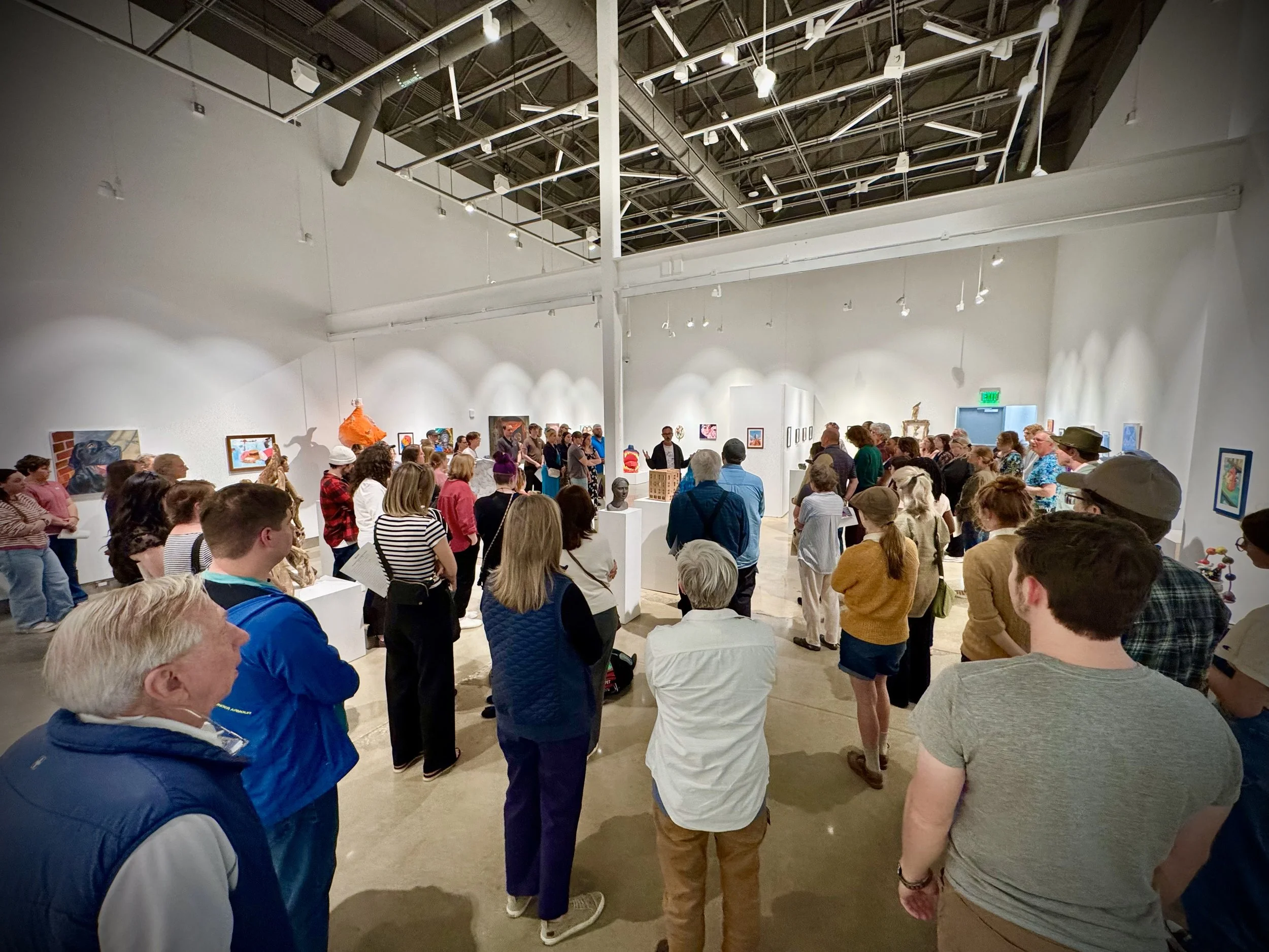  A crowded art gallery space filled with visitors attending an opening reception. 