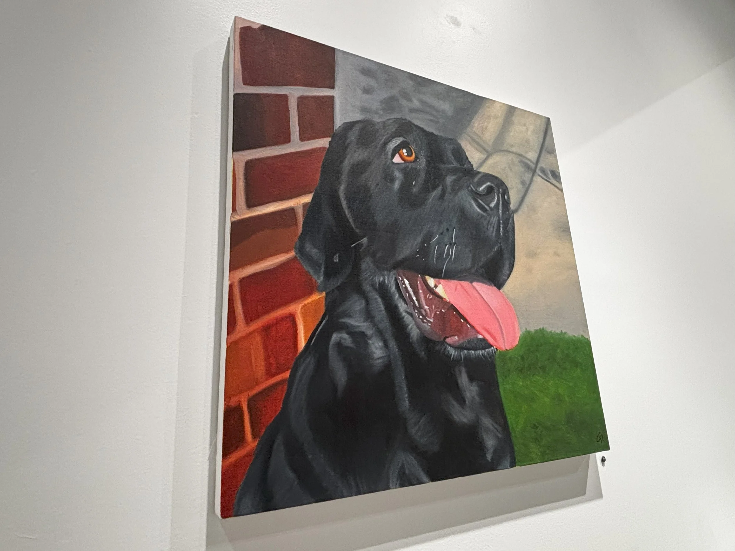  A close-up side perspective of a square canvas painting featuring a happy black Labrador Retriever. 