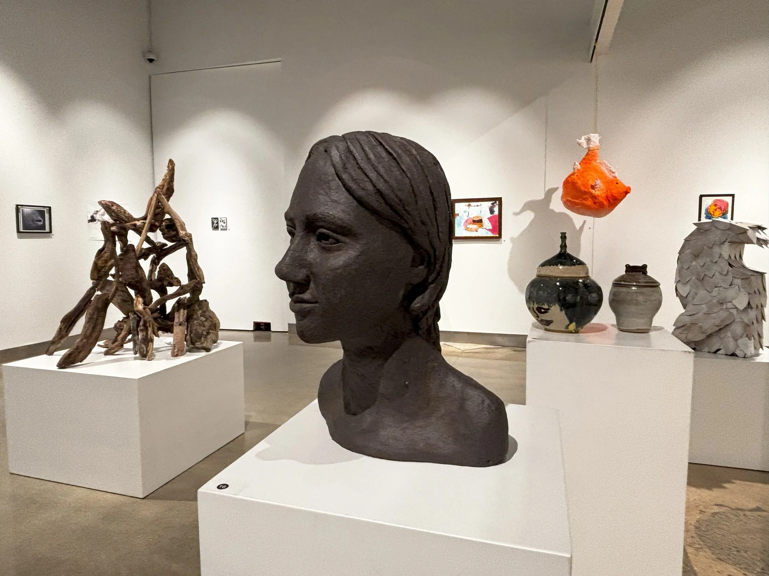  A dark ceramic bust sculpture of a person's head and shoulders shown in profile on a white pedestal. 