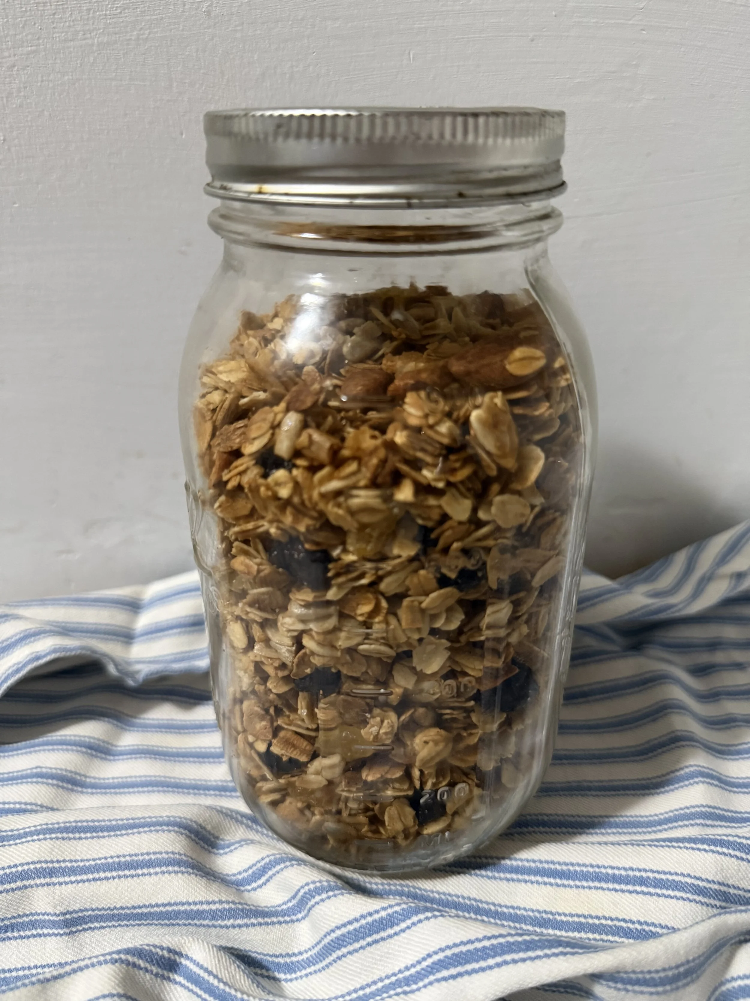 A glass jar filled with granola on a striped kitchen towel