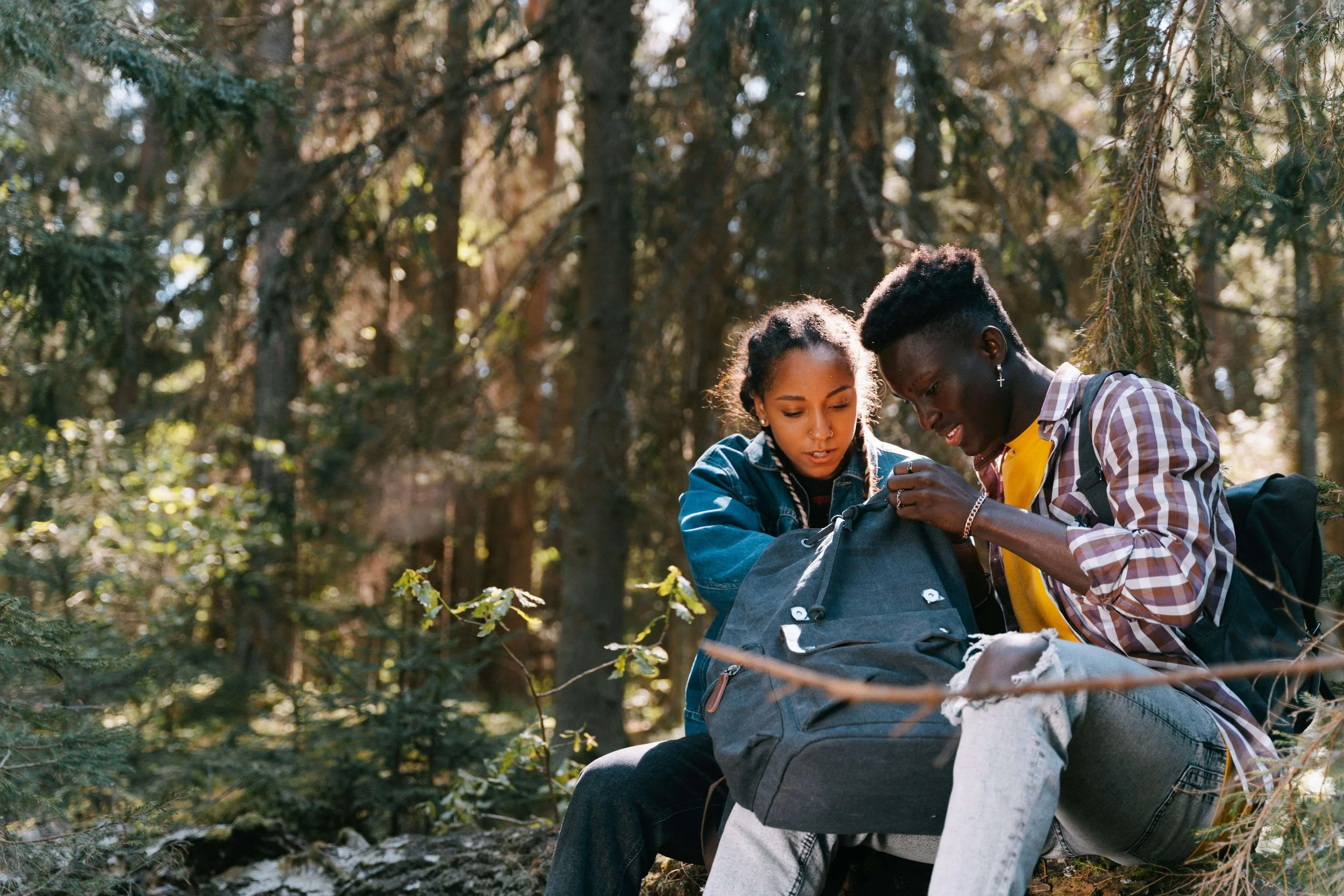 Queer couple sitting in the woods looking into a backpack together, symbolizing partnership, collaboration, and the kind of steady support offered through Minneapolis couples therapy and queer couples therapy near me.