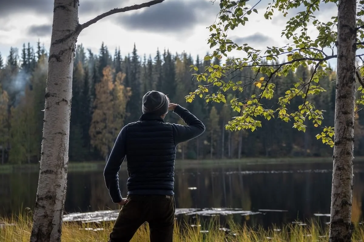 Person standing at the edge of a lake gazing out toward the treeline, representing reflection and the forward-looking work of religious trauma therapy and cult recovery in St. Paul, MN.