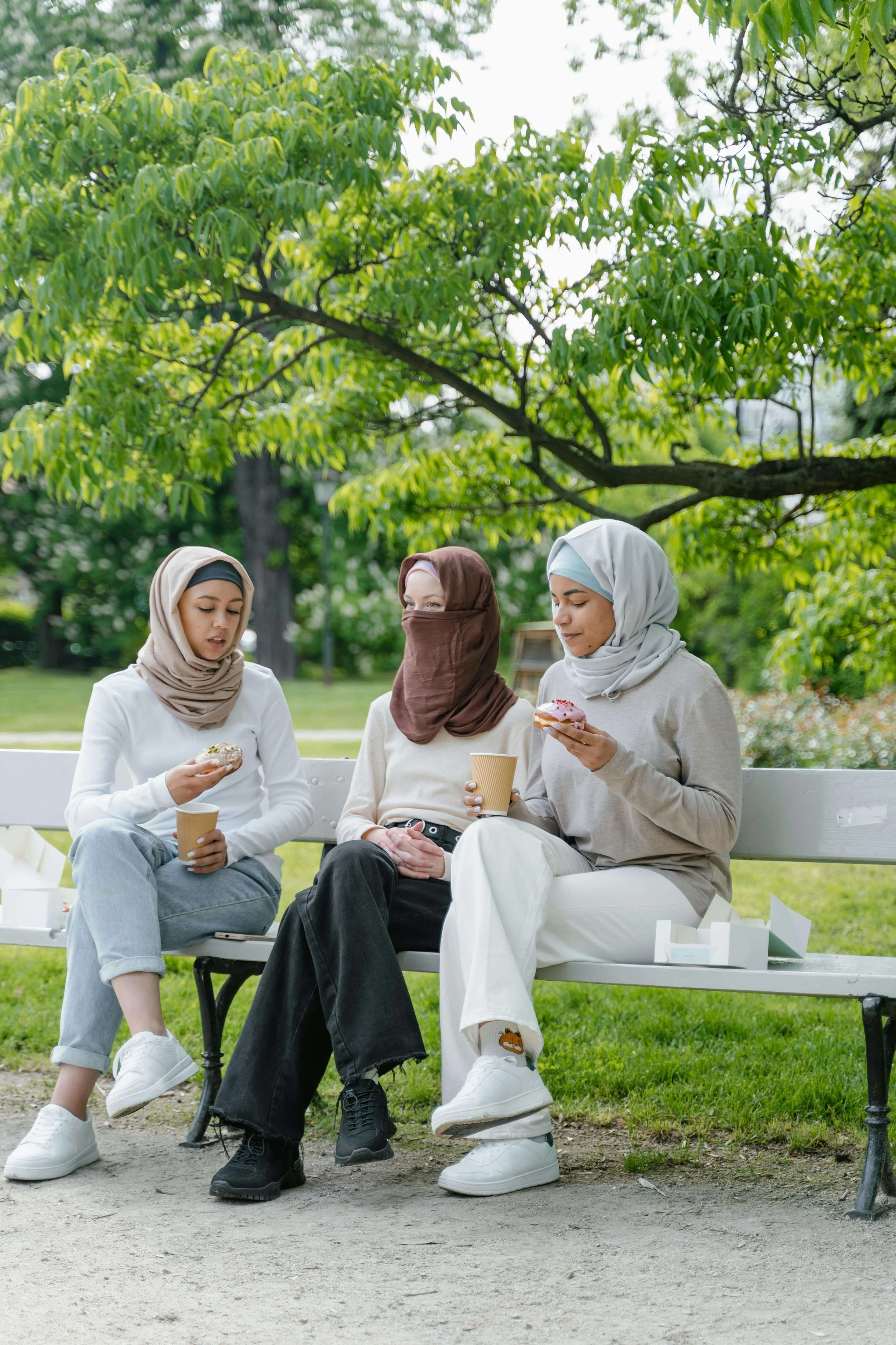 Three women in hijabs sitting together on park bench, representing community and healing from adverse religious experiences in Minnesota with a religious trauma therapist in St. Paul.