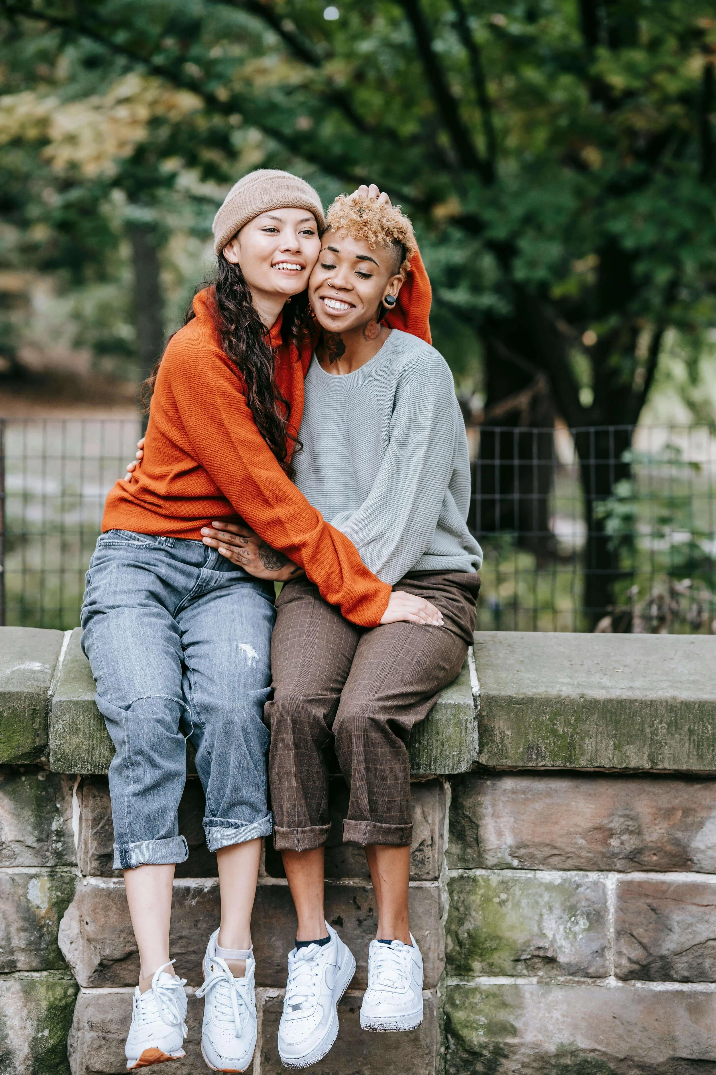 Two women embracing and smiling together outdoors, representing healing and authentic connection with a spiritual trauma therapist in St. Paul, MN, through somatic queer couples therapy in Minneapolis, MN.