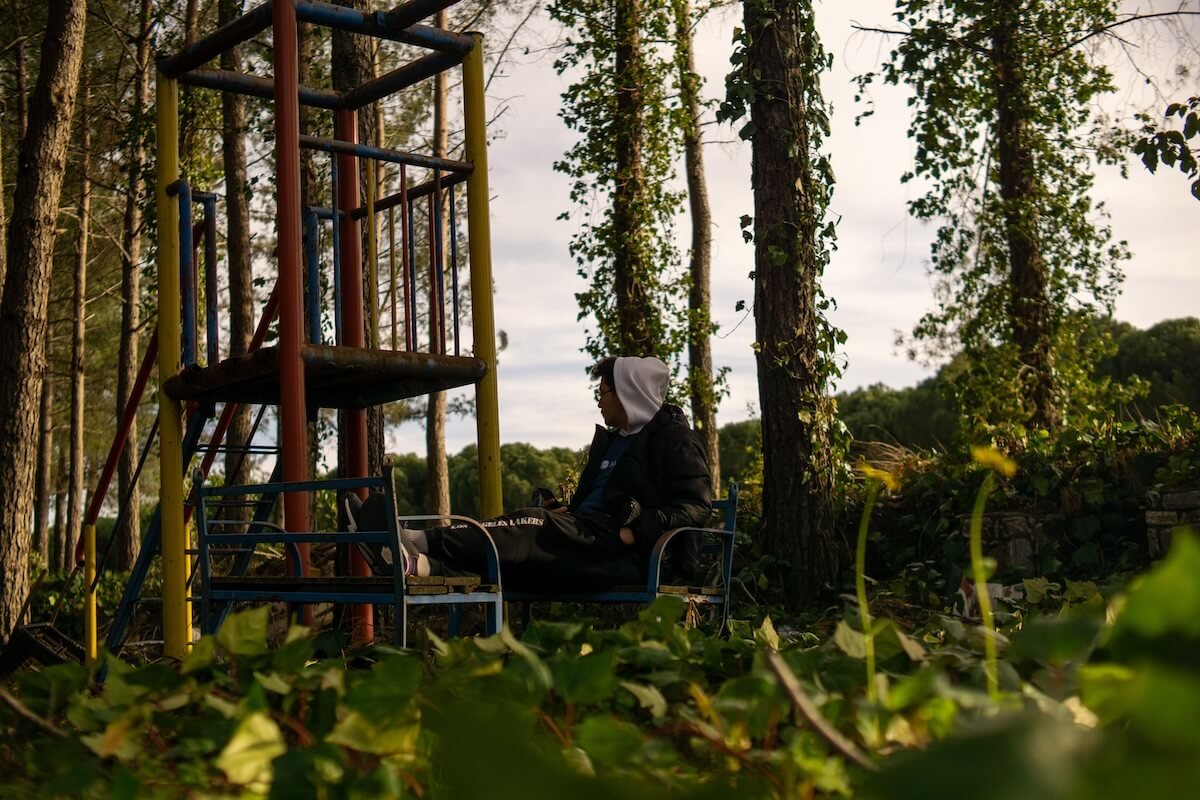 Person sitting alone on a bench beside an old playground in the woods, representing quiet reflection and the healing journey through religious trauma therapy with a religious trauma therapist in St. Paul.