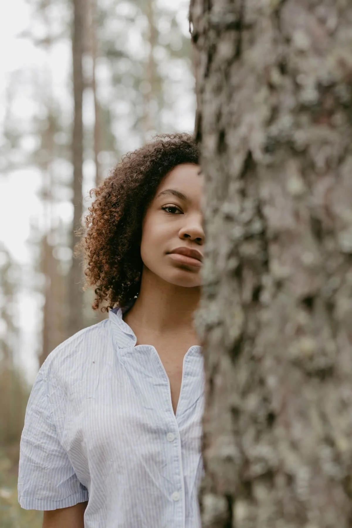 Woman standing beside a tree in the forest, looking calmly at the camera, representing self-reflection and steadiness through religious trauma counseling and repair after conflict in St. Paul.