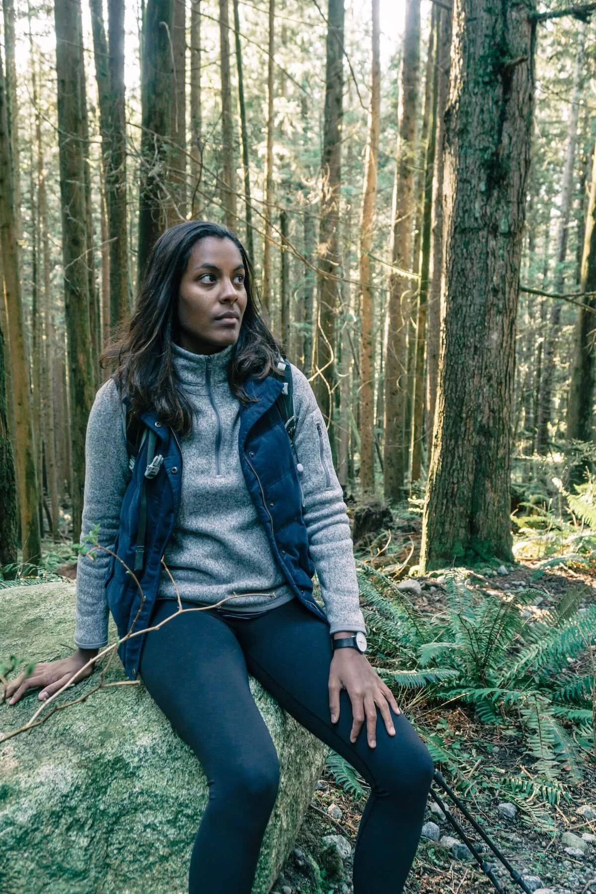 Woman sitting on a rock in the forest looking thoughtfully into the distance, representing reflection and queer religious trauma healing in St. Paul through spiritual trauma therapy.