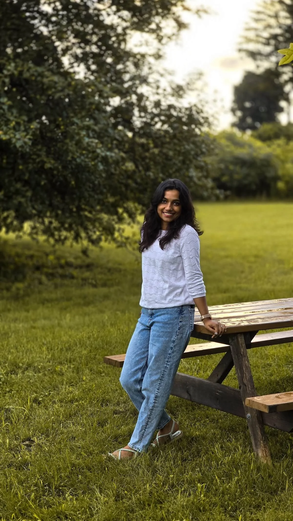 Woman smiling while leaning against a picnic table in a sunlit park, representing authenticity and self-acceptance through healing religious trauma in Minnesota and building relationship repair skills in St. Paul, MN.