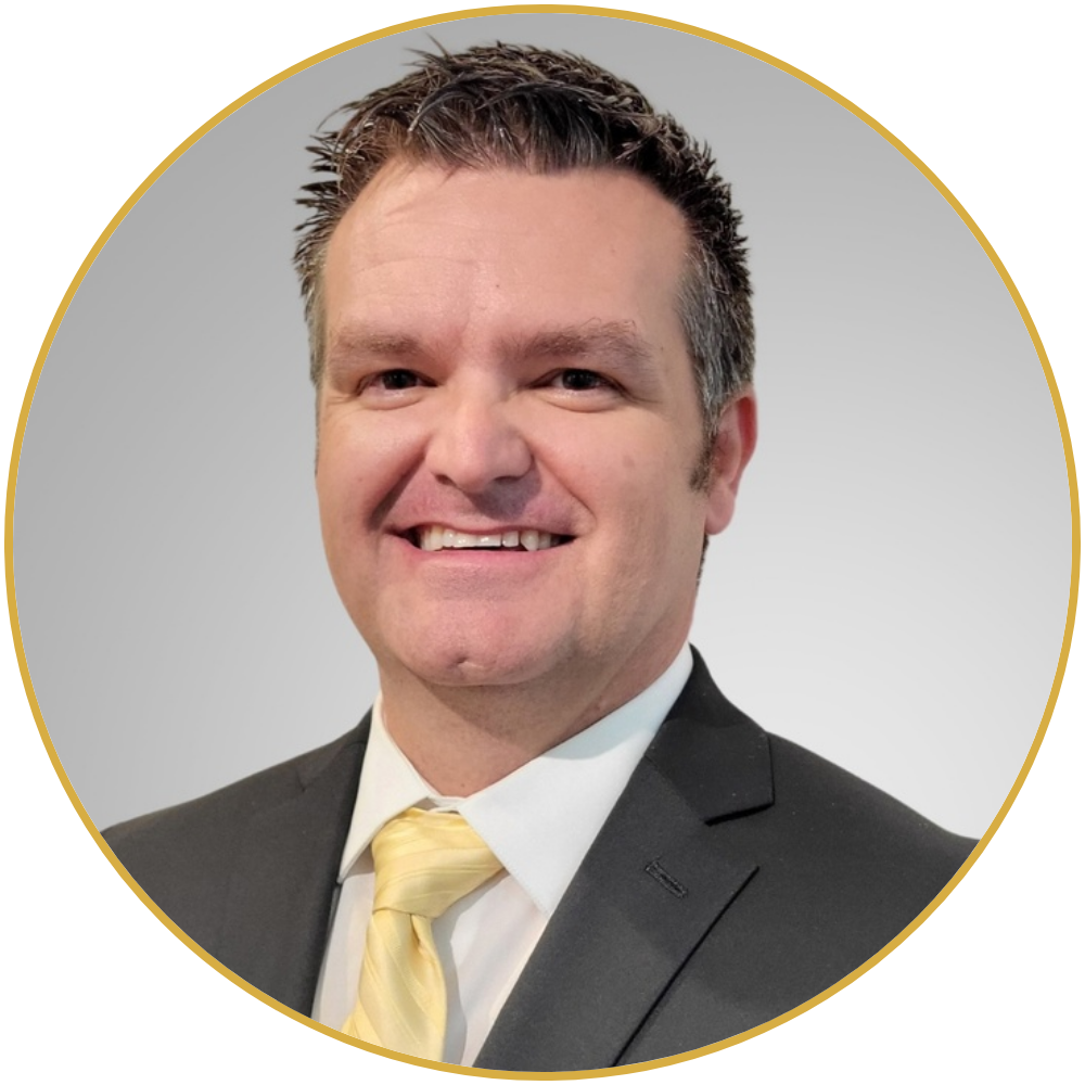 A professional headshot of a man in a black suit, white shirt, and yellow tie, smiling against a plain light gray background.