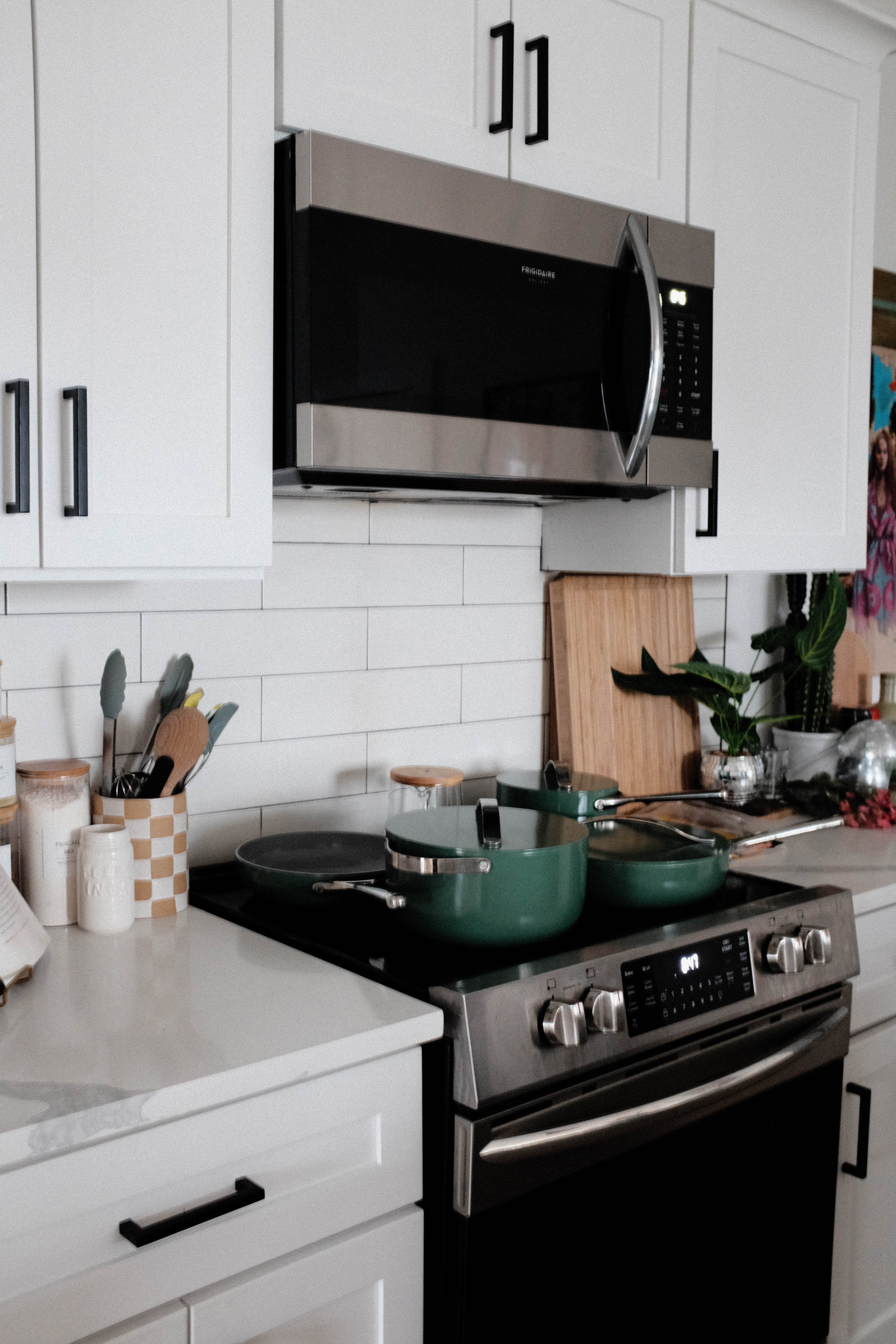 Modern kitchen with white cabinets, stainless steel microwave, black stove with two green pots, and various kitchen utensils.