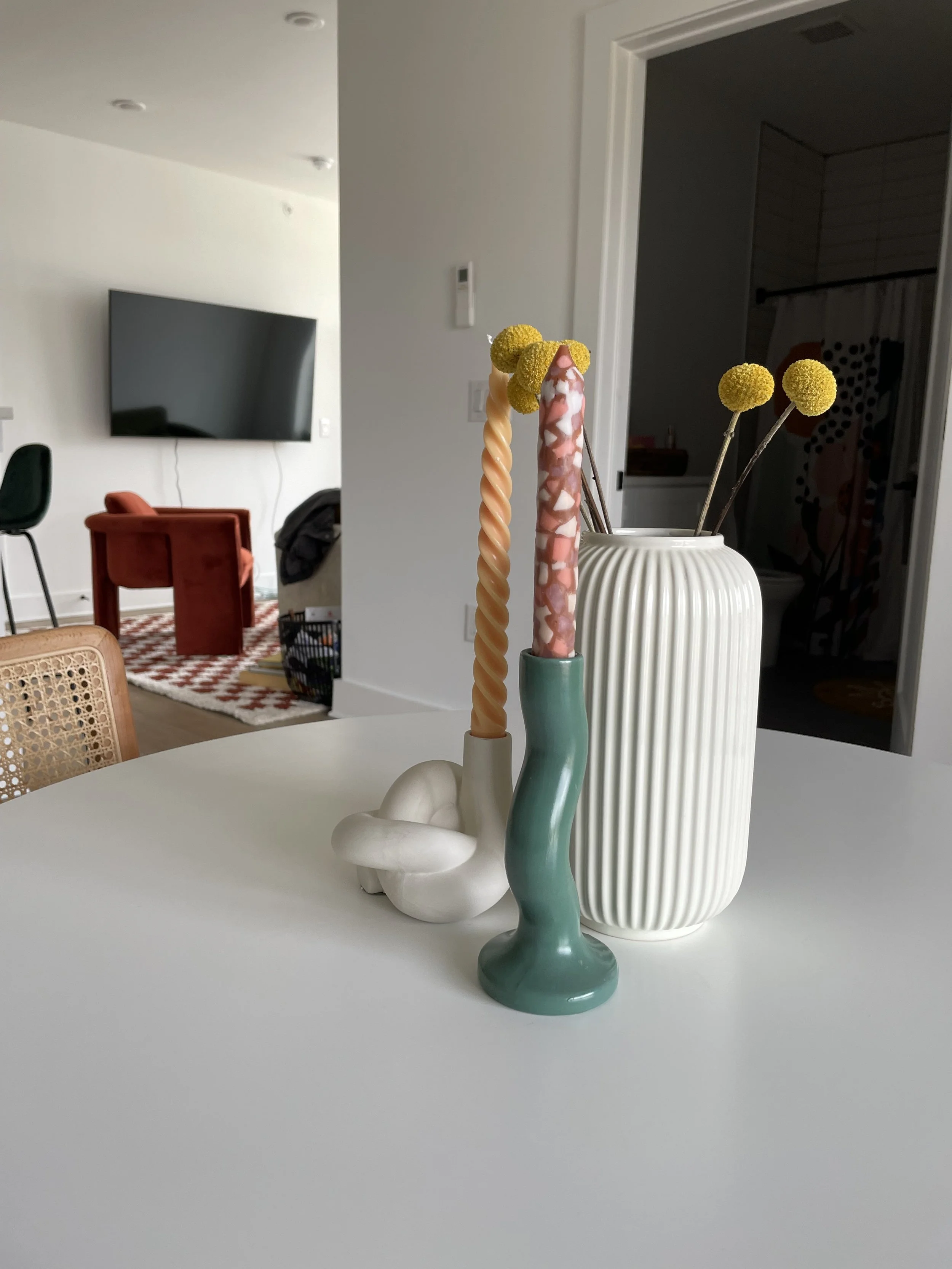 Decorative candles and a vase with yellow billy ball flowers on a white table in a modern home interior.