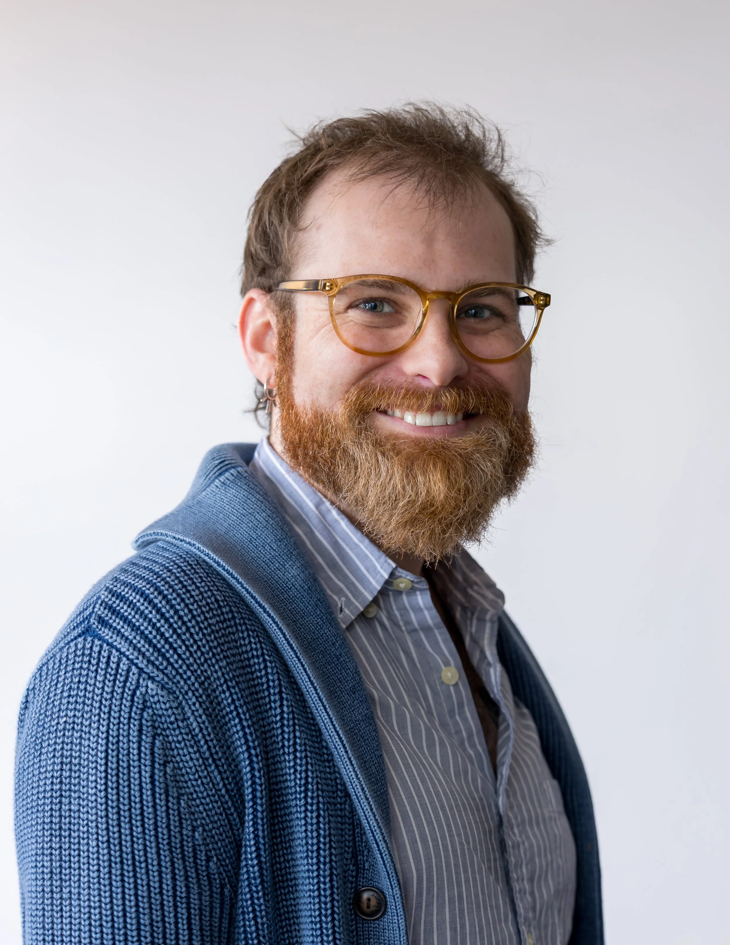 A smiling man with glasses and a beard wearing a colorful, abstract-patterned shirt.
