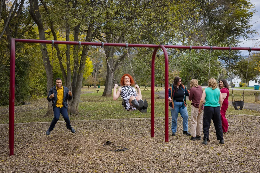 People spending time together at a playground, with two on the swings and others talking nearby.