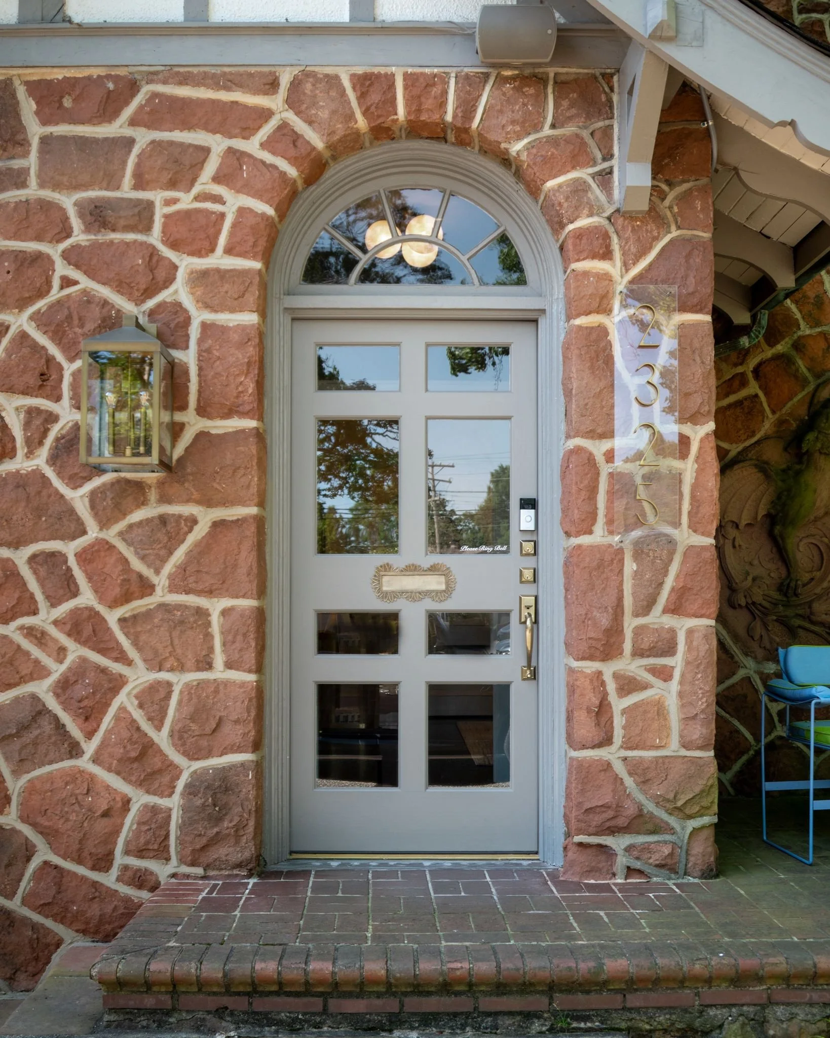 An exterior shot of a grey front door with 8 panes of glass, and antique brass hardware