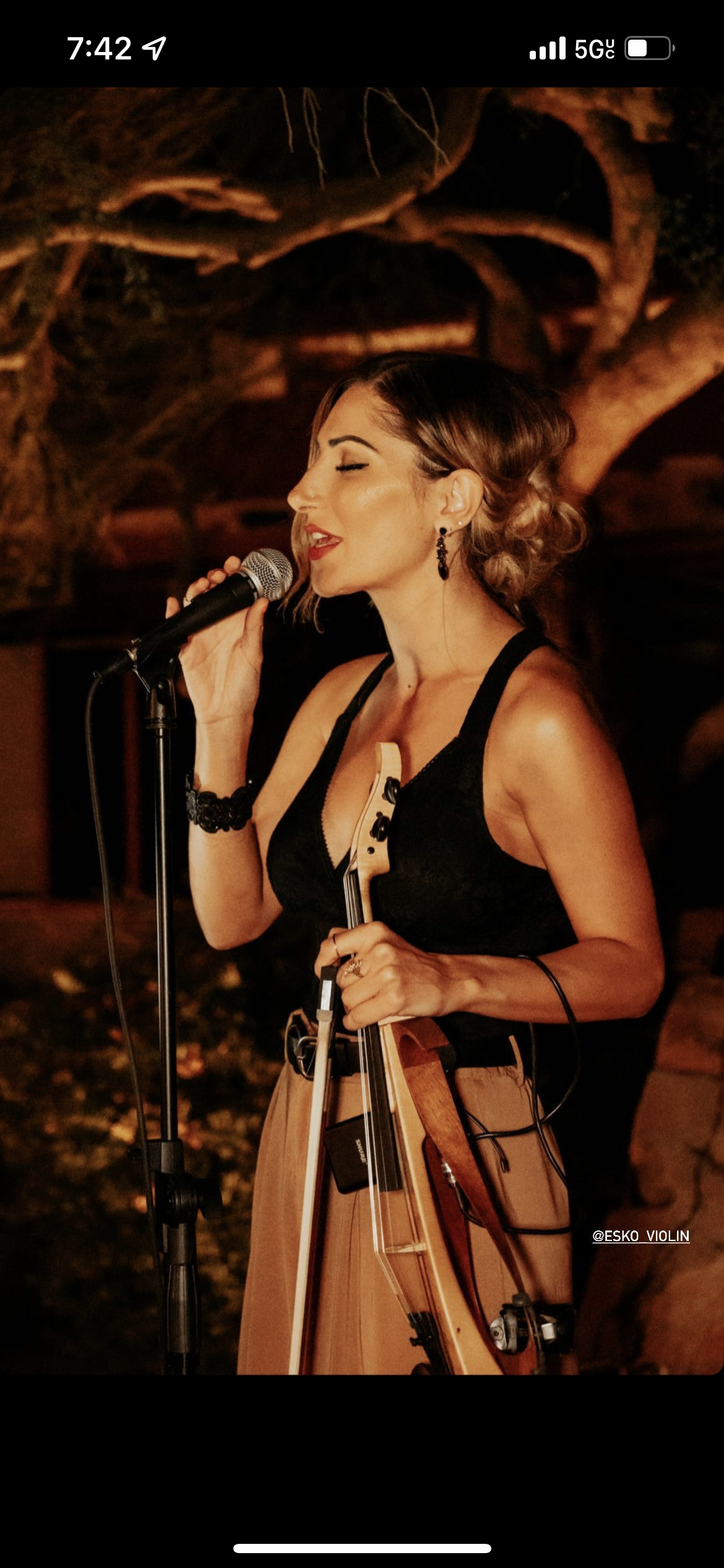 A woman singing into a microphone while holding a violin.