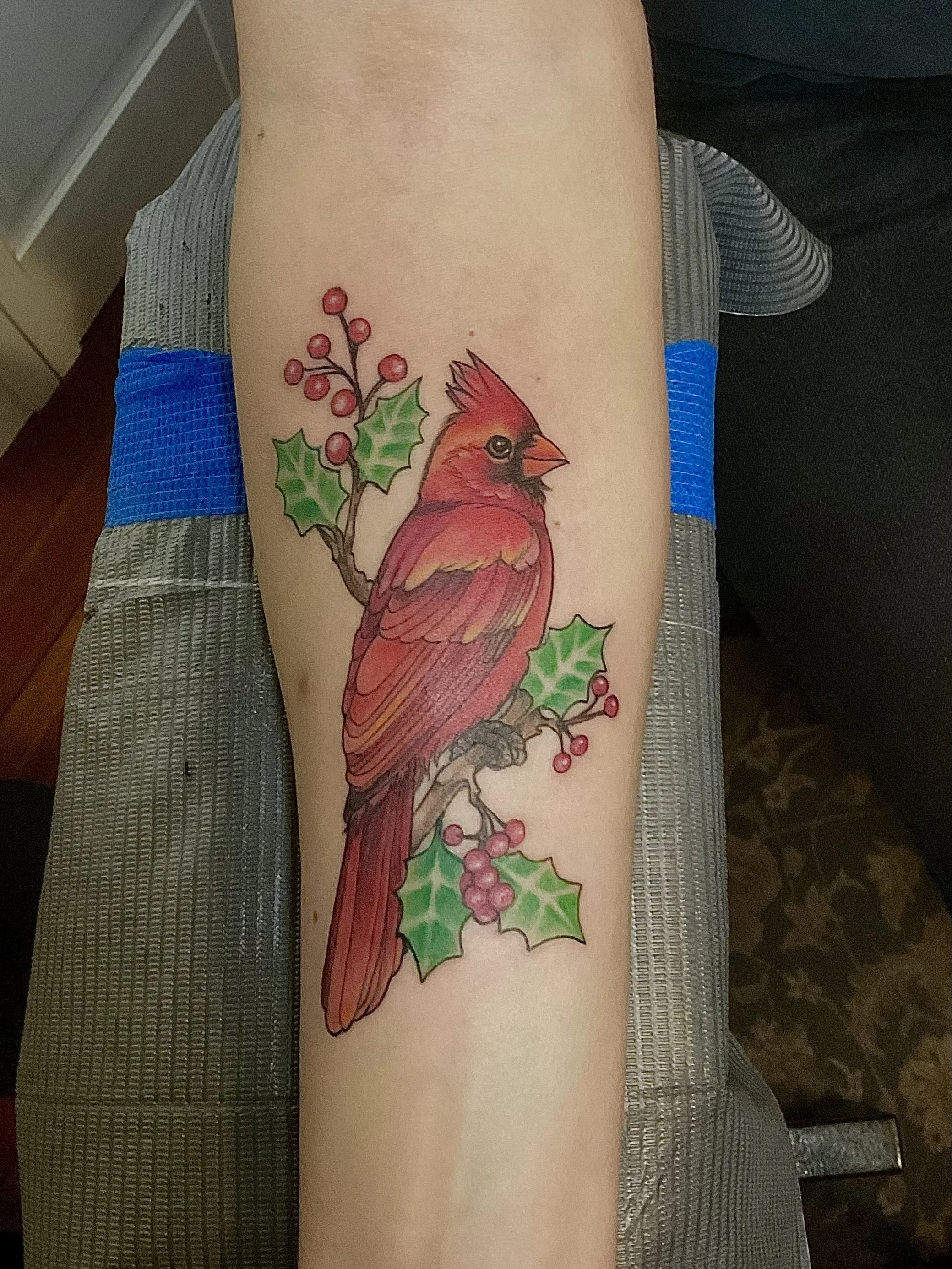 Tattoo of a red cardinal bird on a holly branch on an arm