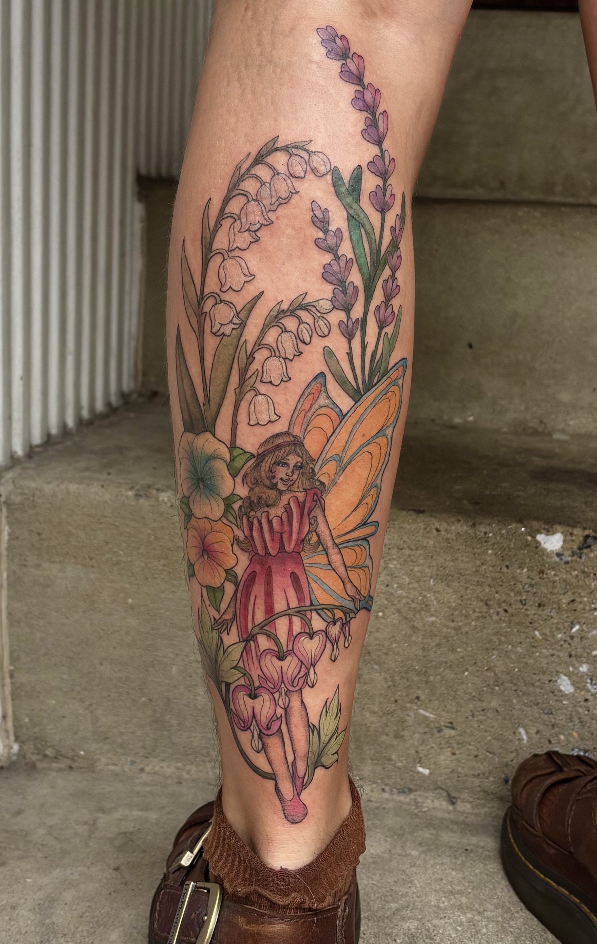 Tattoo of a vintage inspired fairy among lavender, lily of the valley, and magnolia flowers on a leg