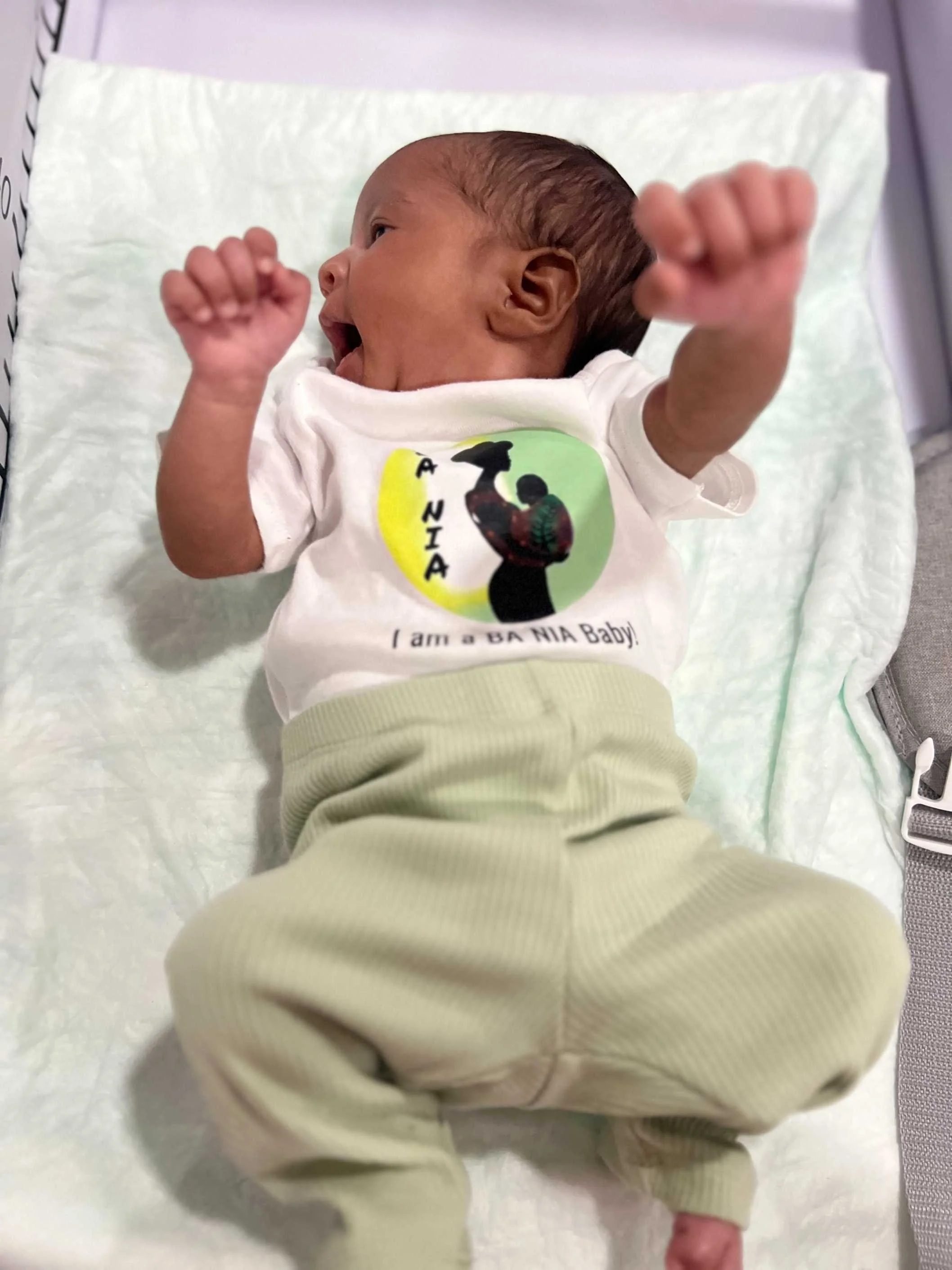 Baby wearing a onesie that says "I am a BA NIA baby!"