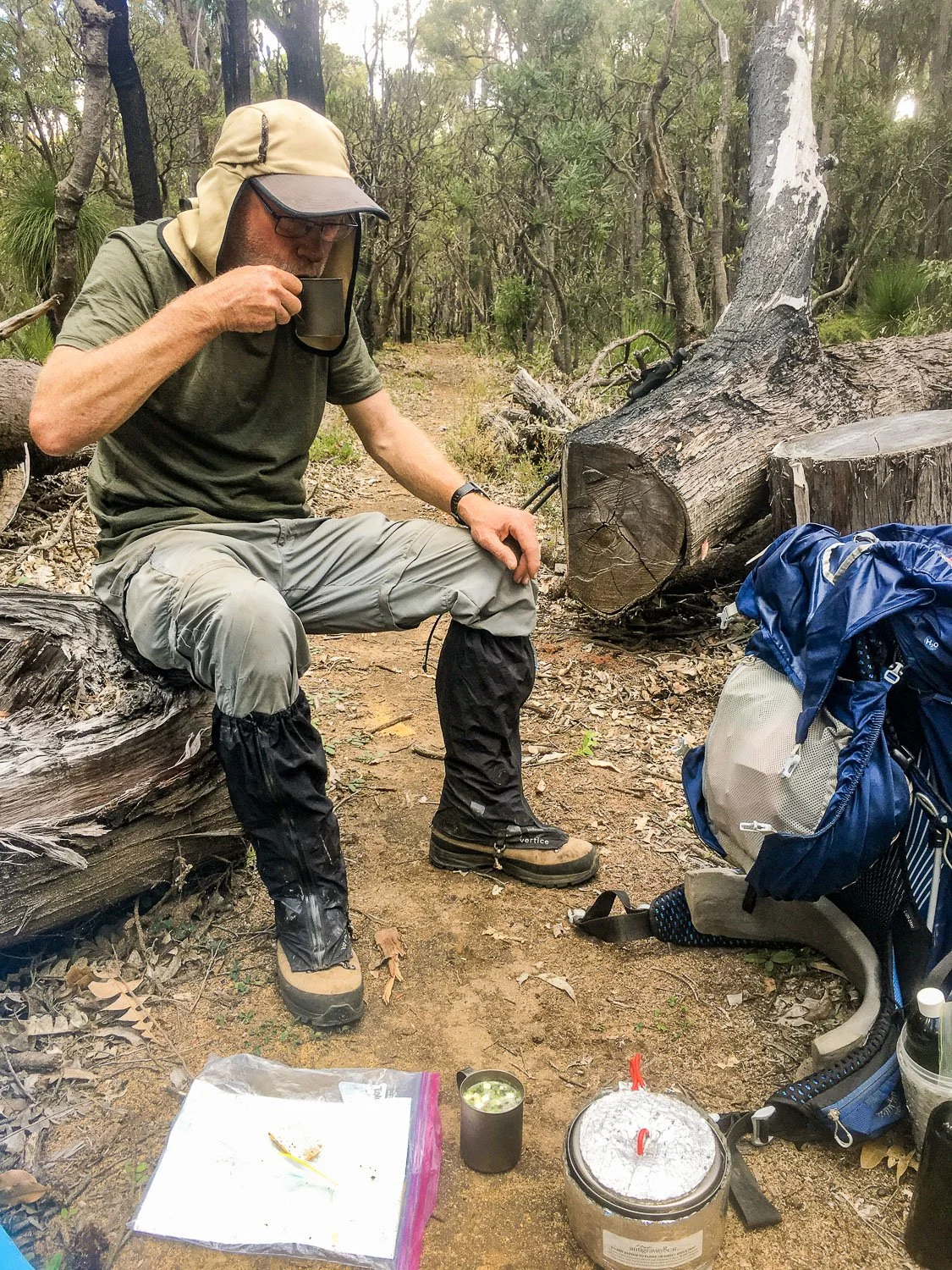 hiker sitting on log having cuppa soup with paper map next to him