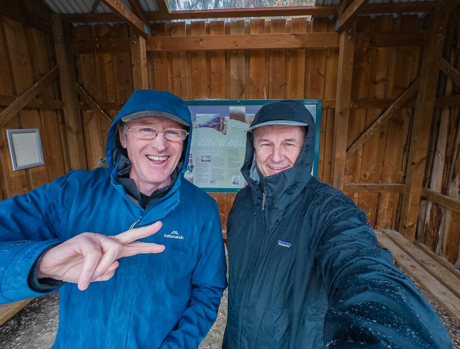 two men in rain jackets one is beading water to other not