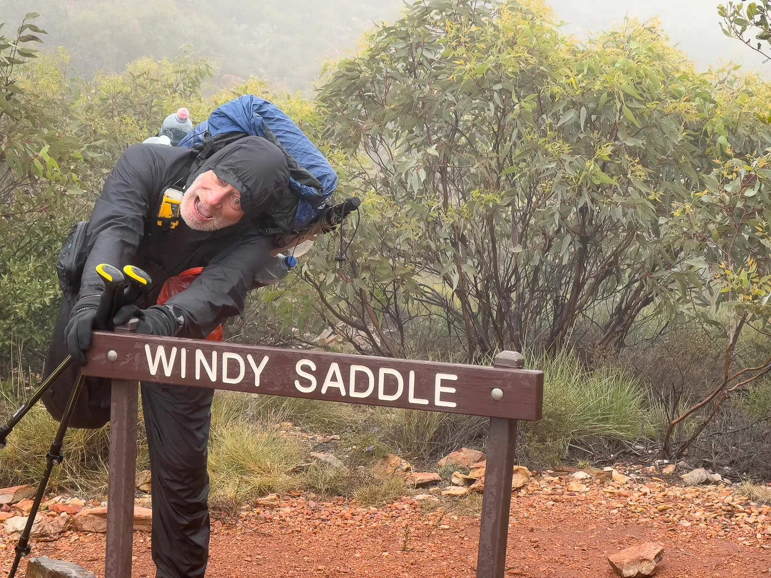 hiker holding ontpo to sign that yes windy saddle pretending to be blown away