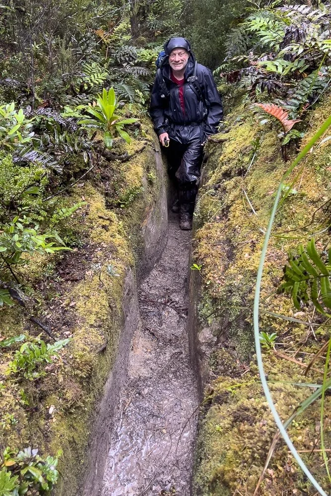 hiker walking along waist deep trench in rain gear thrench is less than 500 millimetres wide