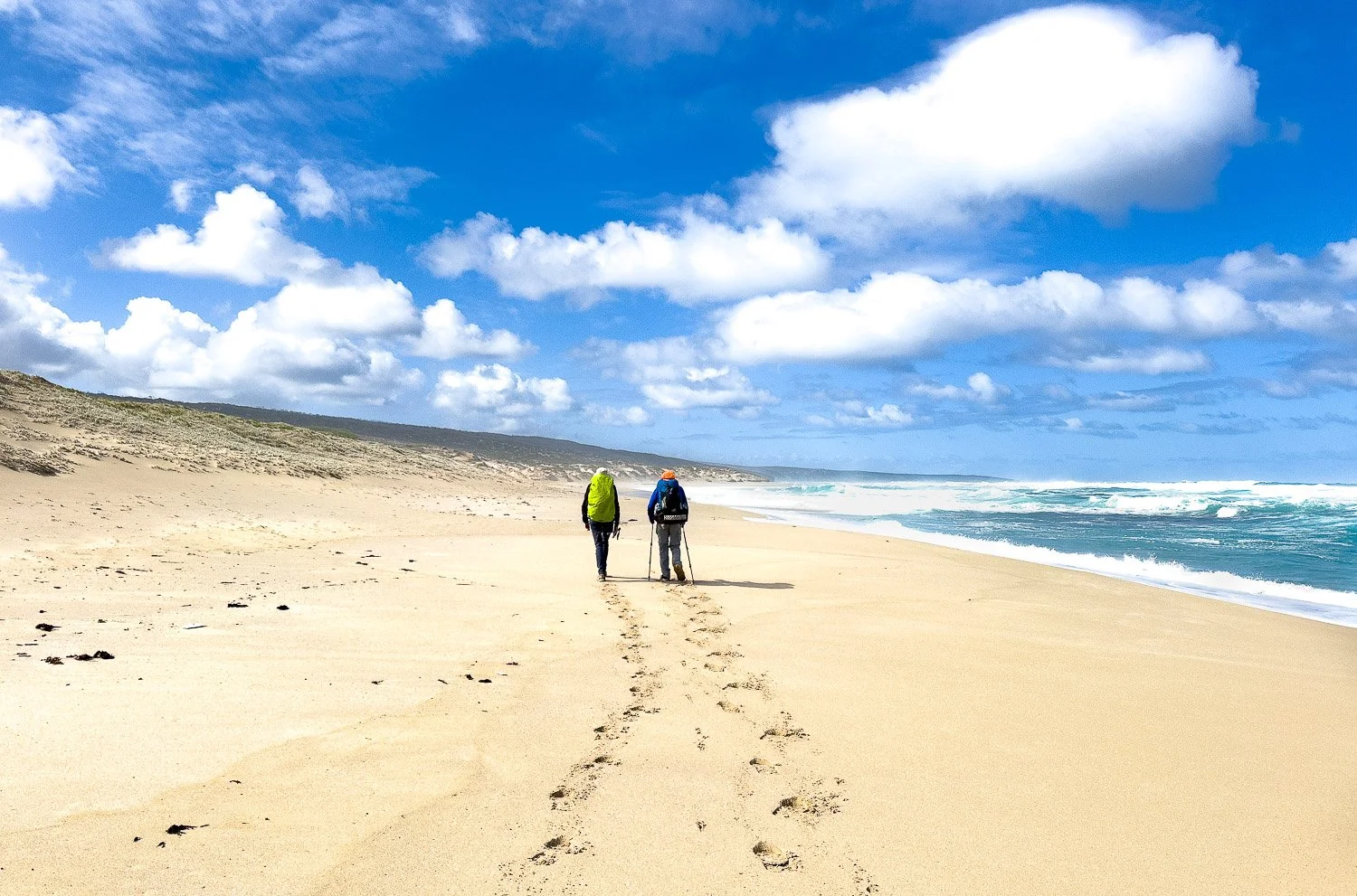 two hikers walking along remote sandy beach