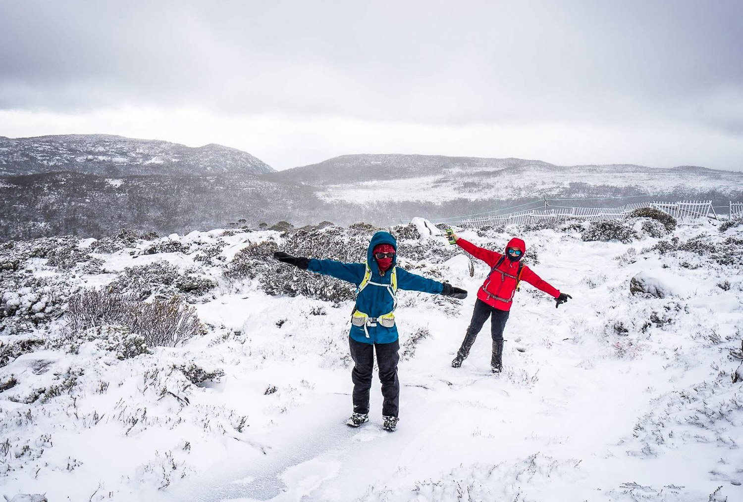 two hikers walking in the snow with their arms stretched out sideways