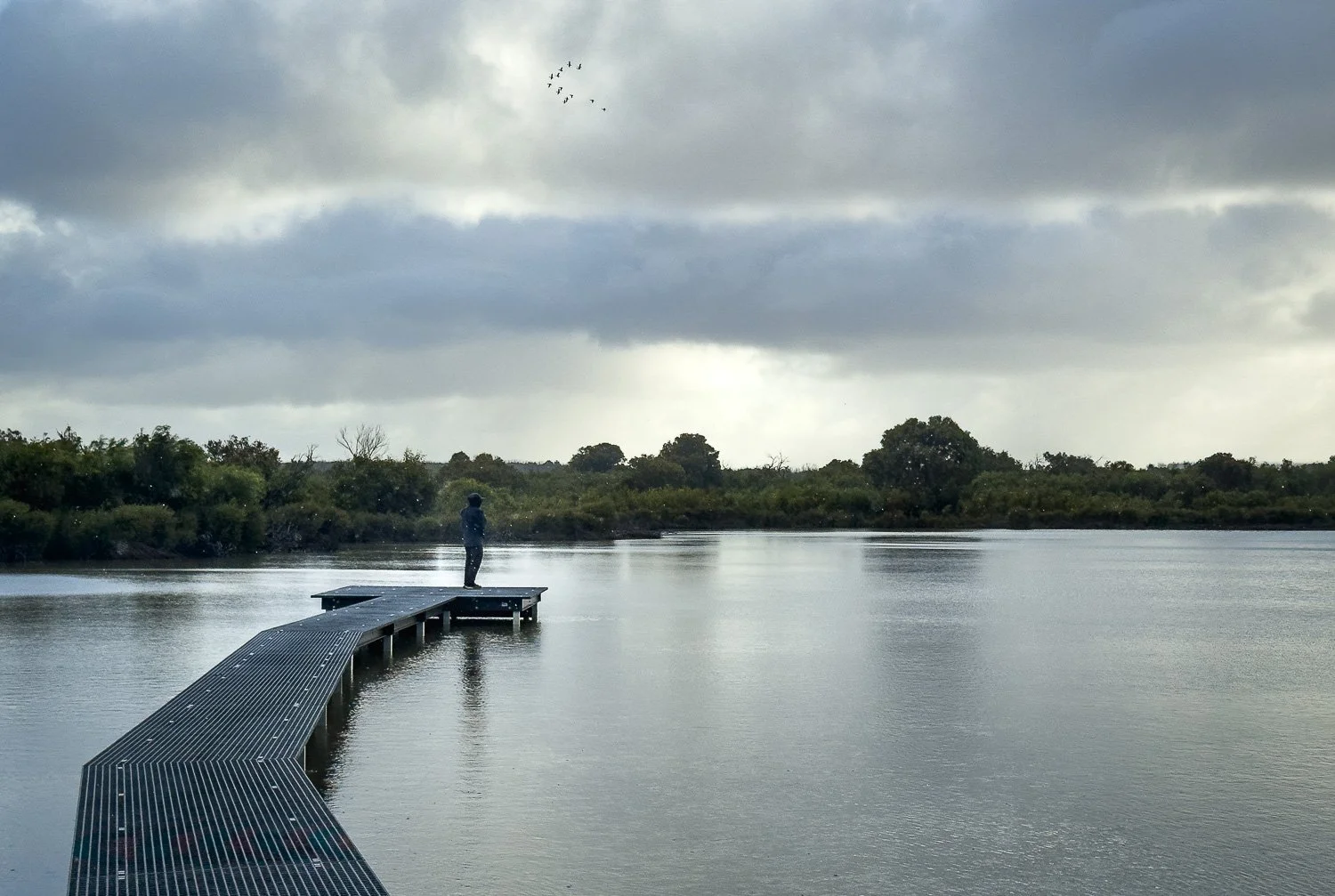 man in rain gear standing at end of small jetty in lake