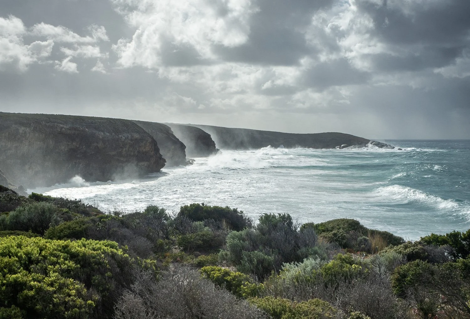 wild sea smashing against cliff with storm clouds above