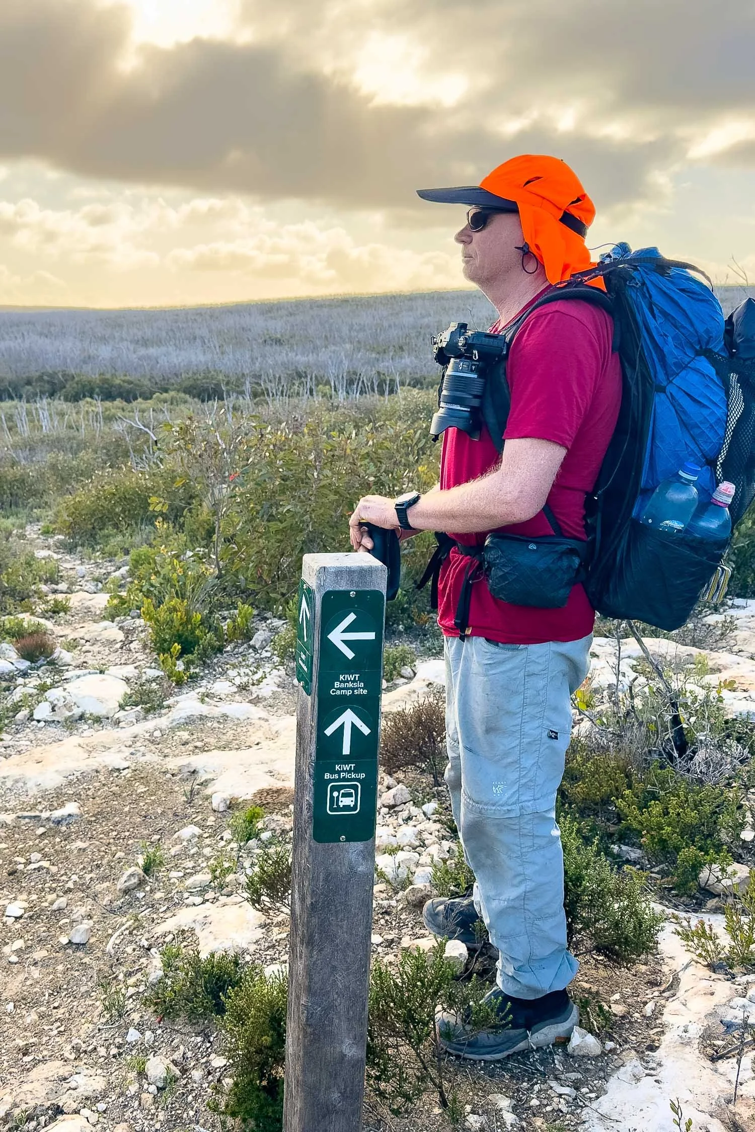 hiker in red shirt with backpack standing upright at bus stop