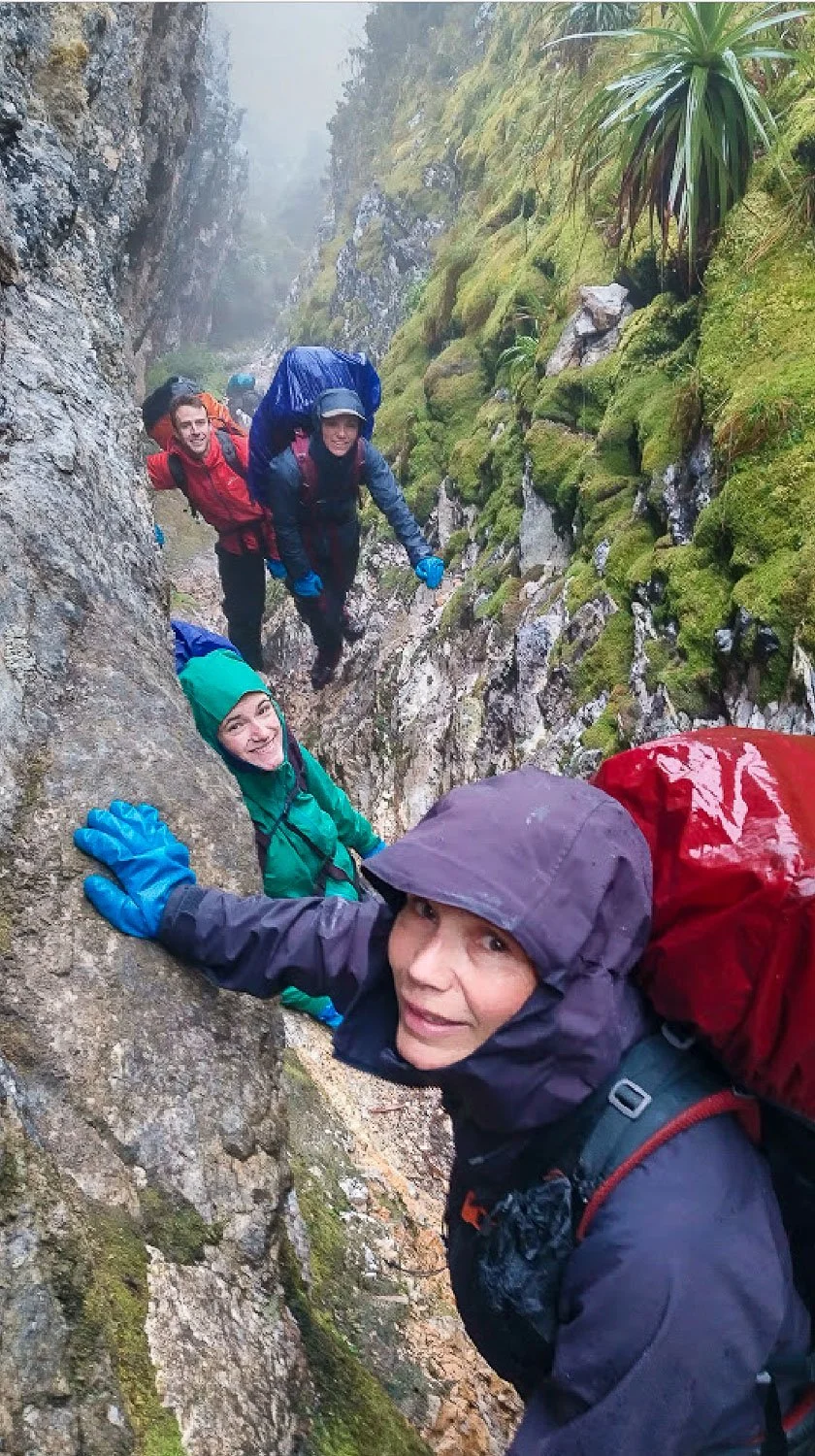 four hikers in rain gear walking through narrow slot in  mountain