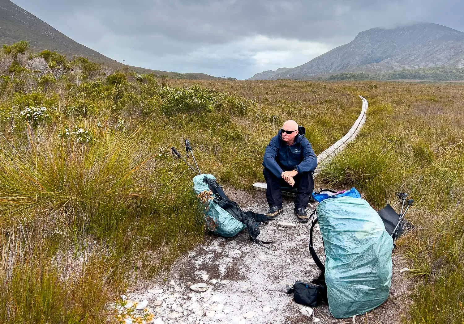 hiker in rain gear sitting on end of duckboard resting